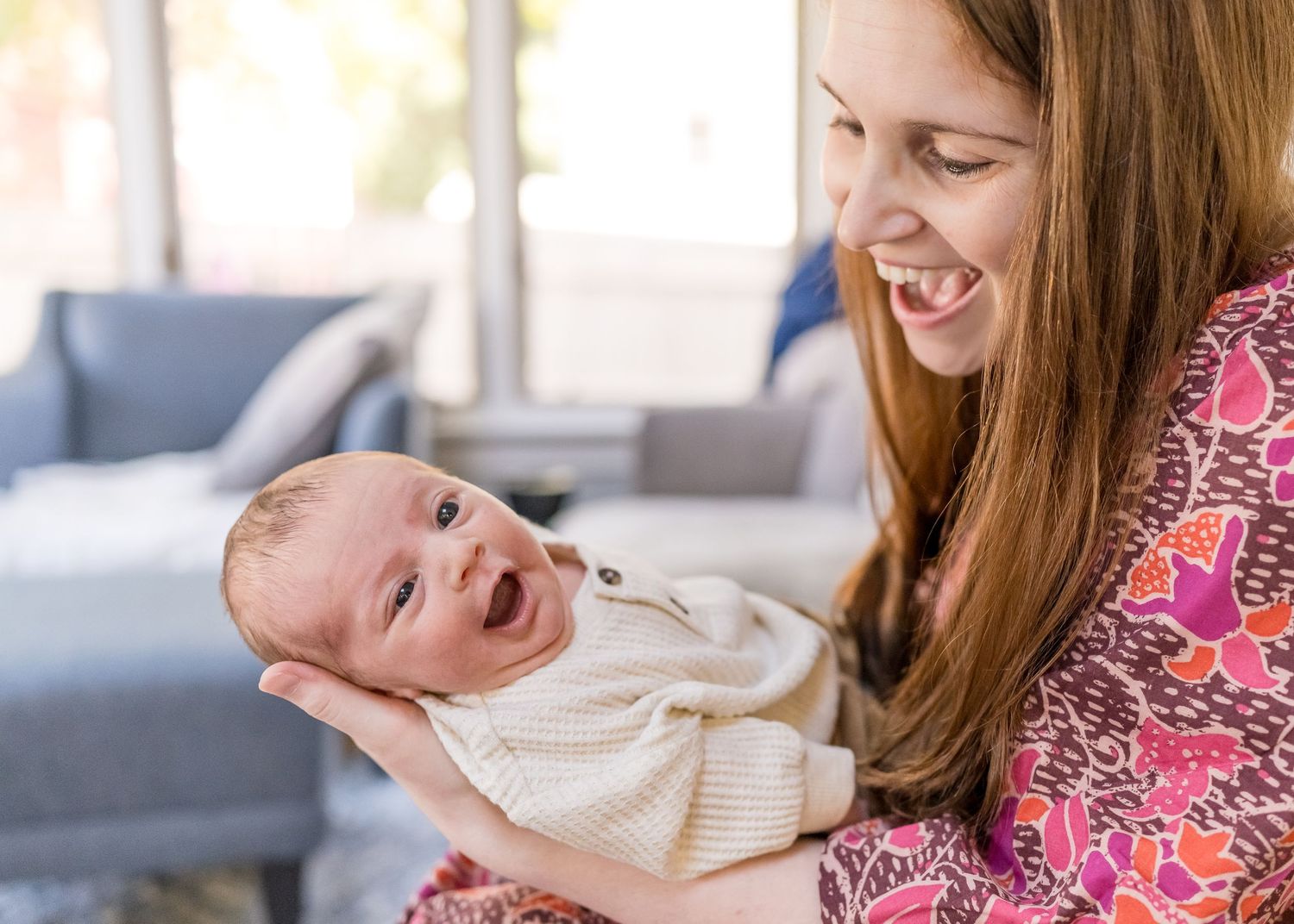 Joyful interaction between mother and laughing baby in white sweater.