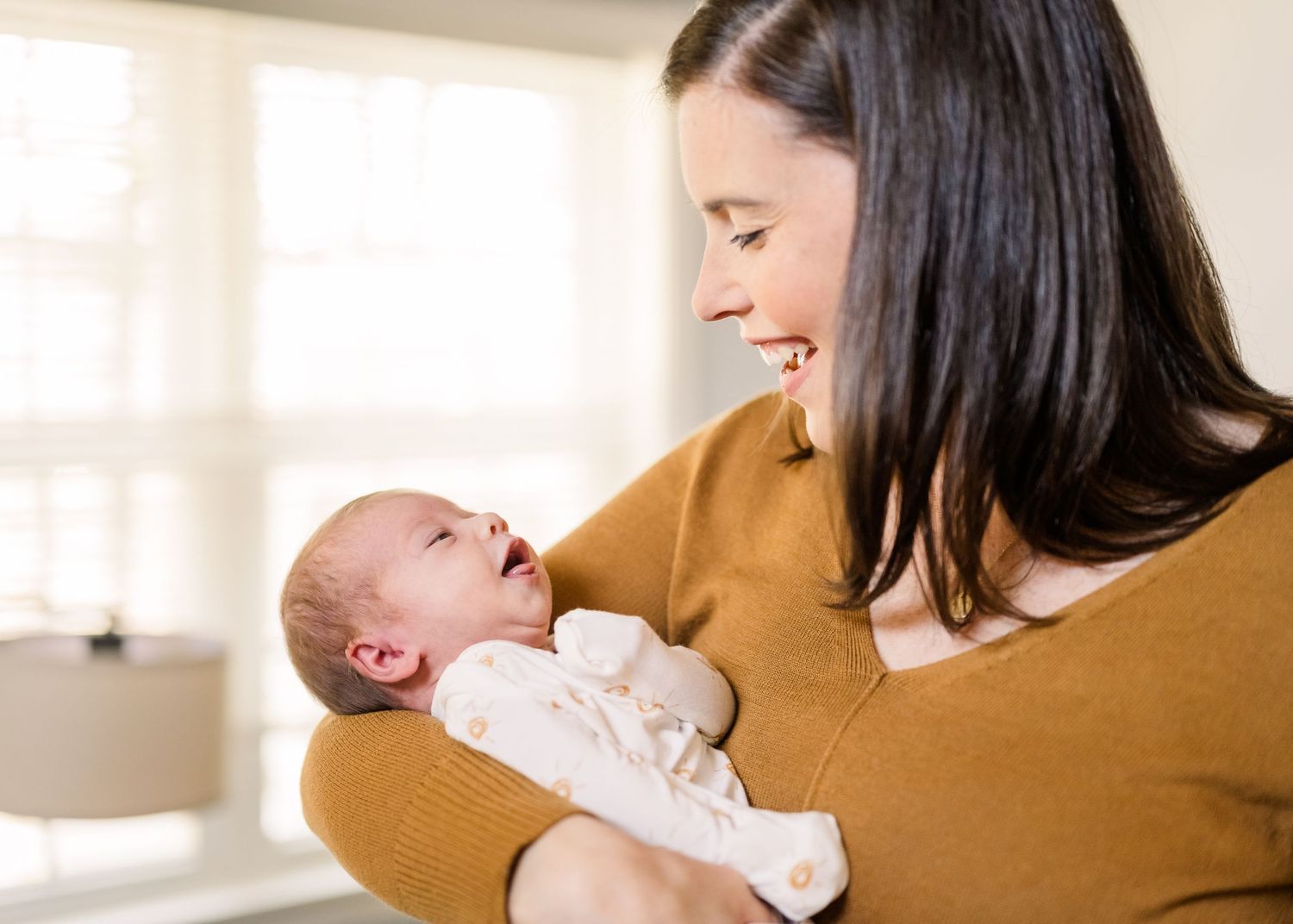 Mother in mustard sweater holding and gazing lovingly at newborn baby.