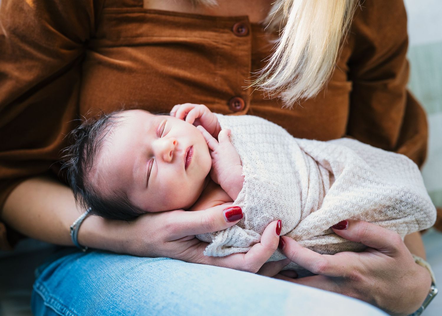 Newborn baby smiling while wrapped in cream colored blanket.