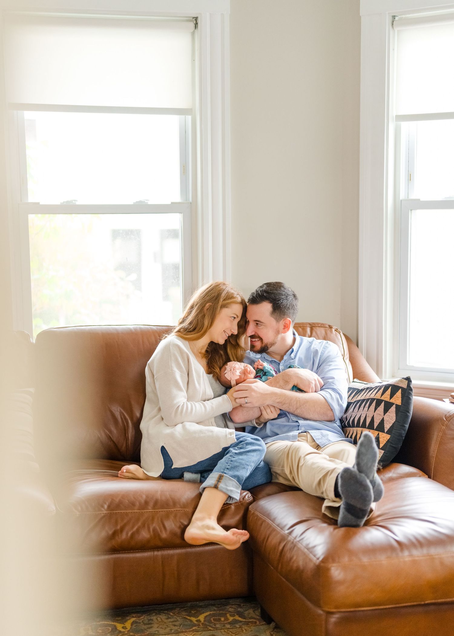 Intimate family moment on brown leather couch by bright windows.