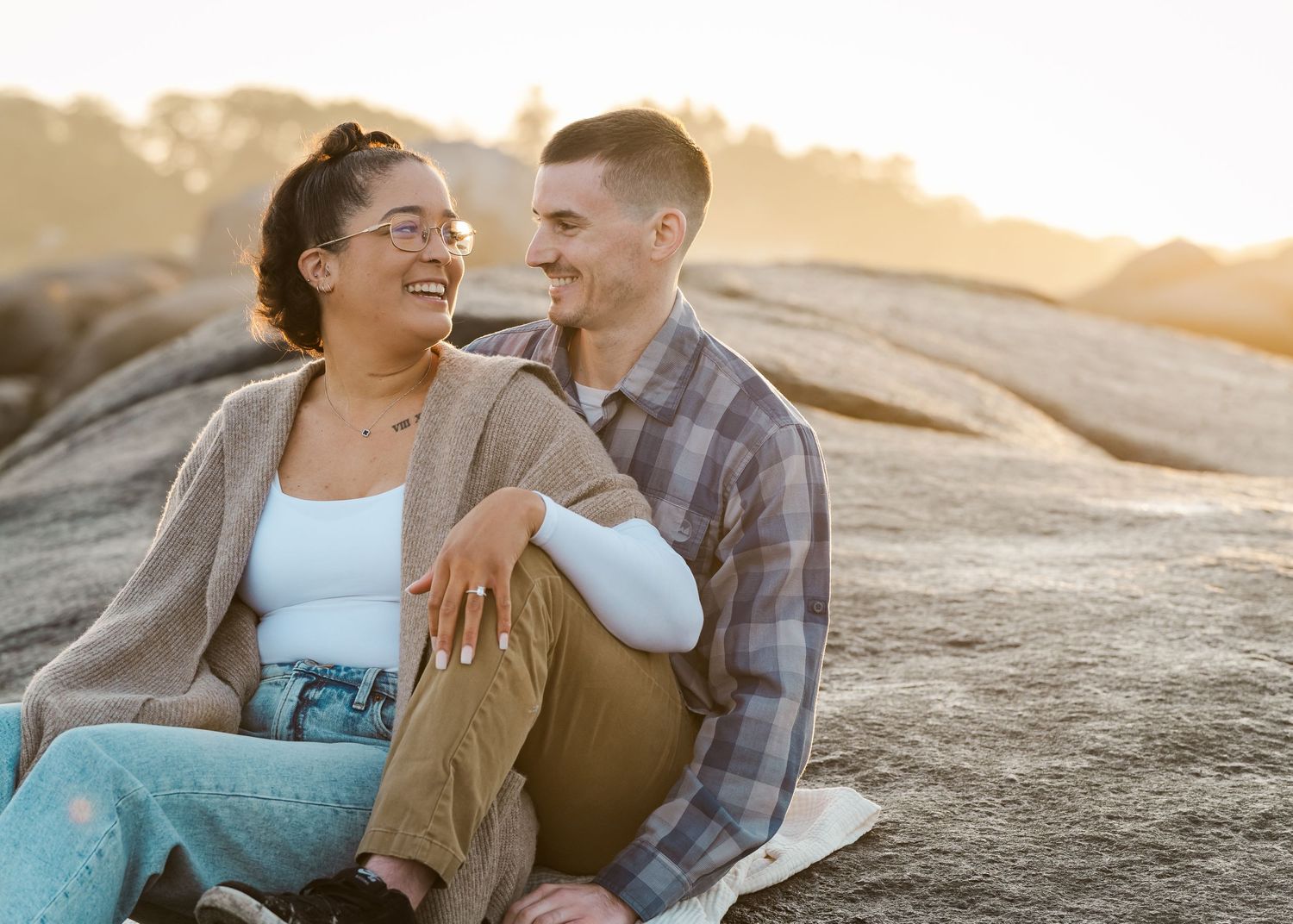 Couple sitting on rocky outcrop during golden hour engagement session.