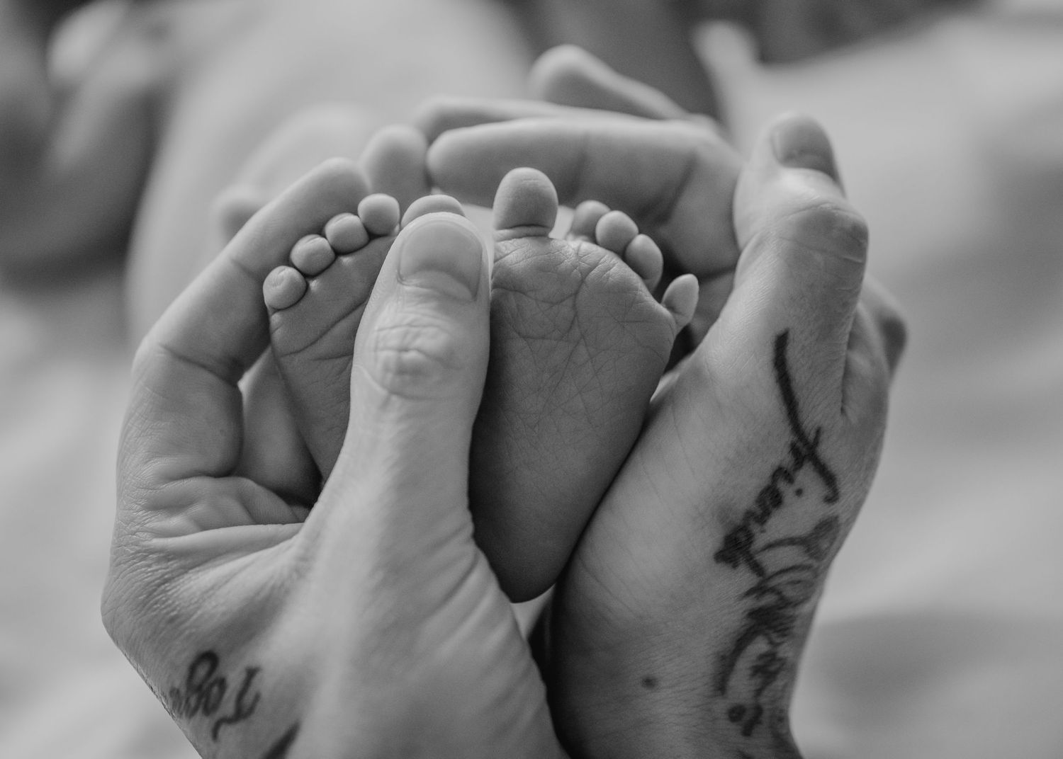 Adult hands gently cradling tiny newborn feet in black and white.