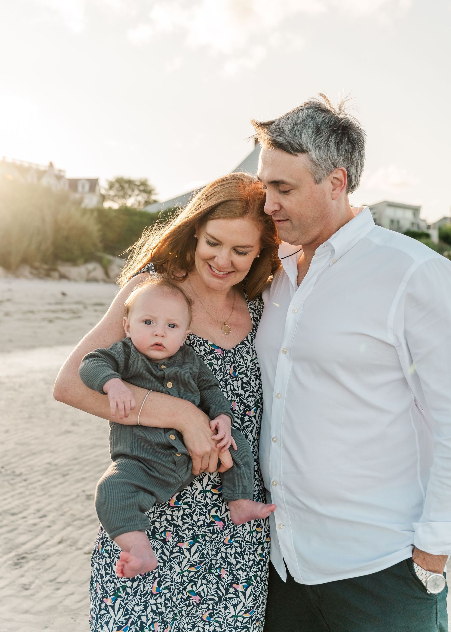 A family shares a tender moment together on the beach at sunset wearing coordinated white and blue outfits.