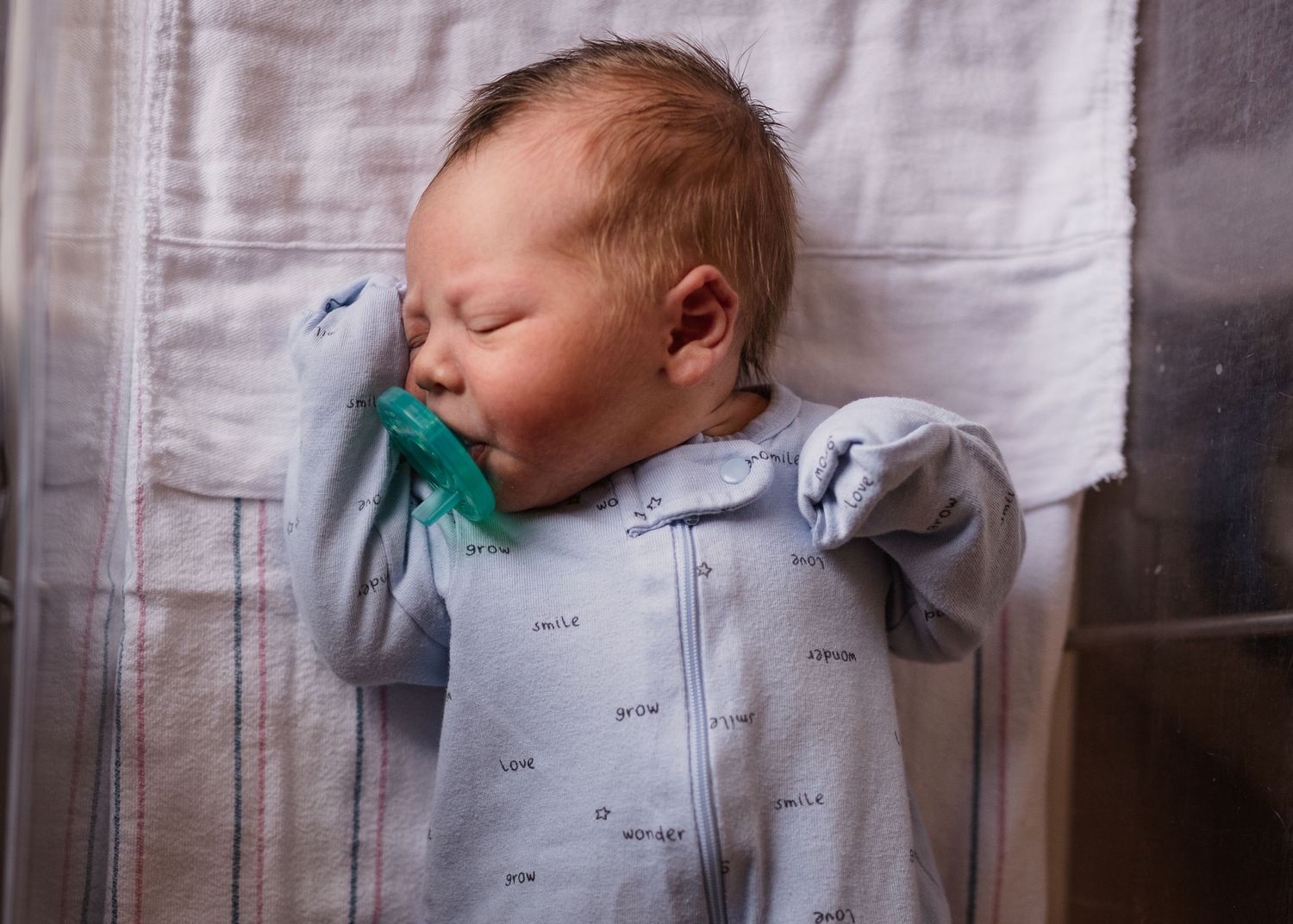 Sleeping newborn with pacifier wearing light blue patterned sleepwear.