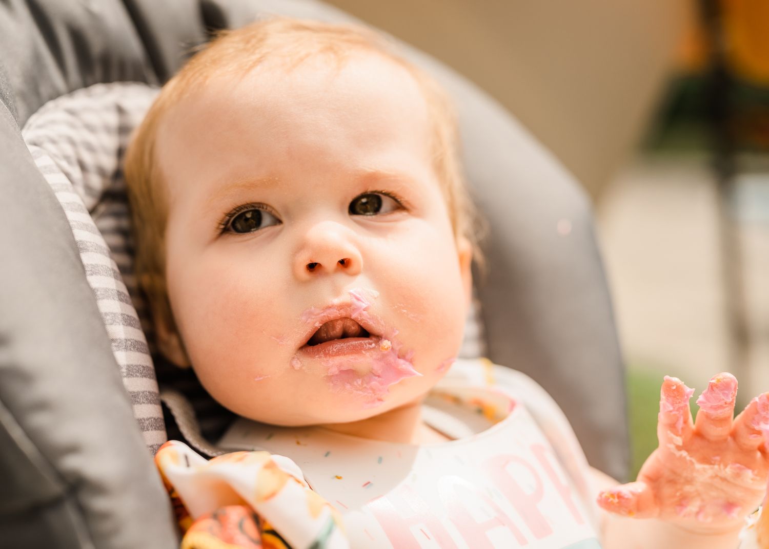 Baby sitting in grey high chair looking up with curiosity.