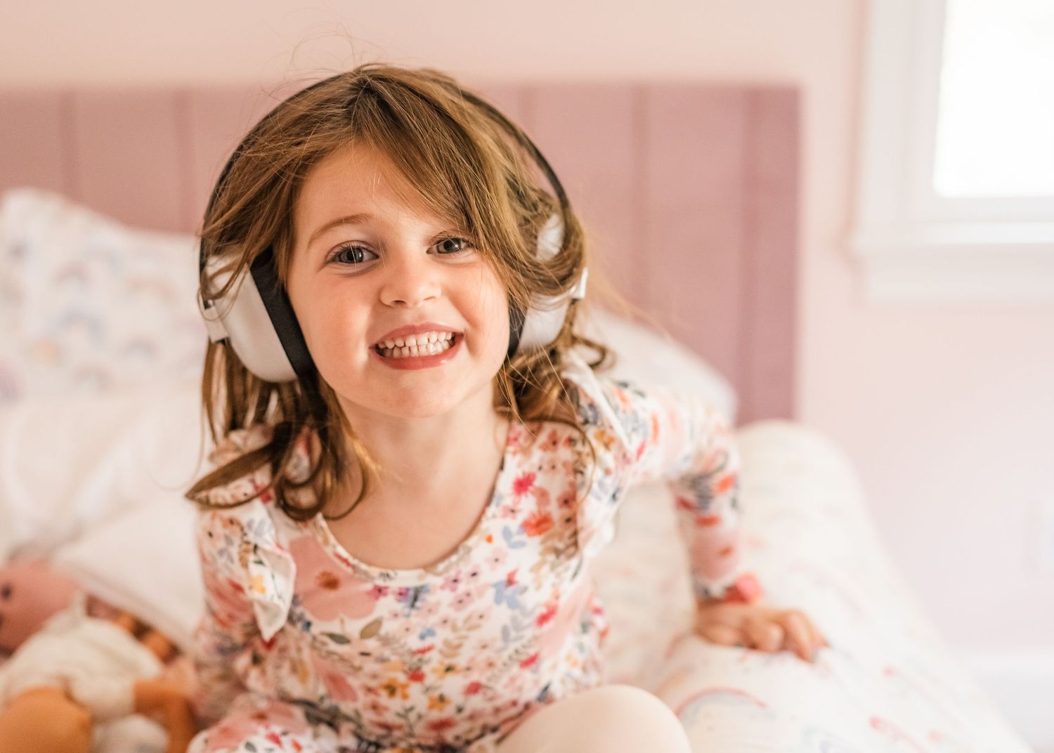 Happy child wearing floral print dress in pink bedroom.