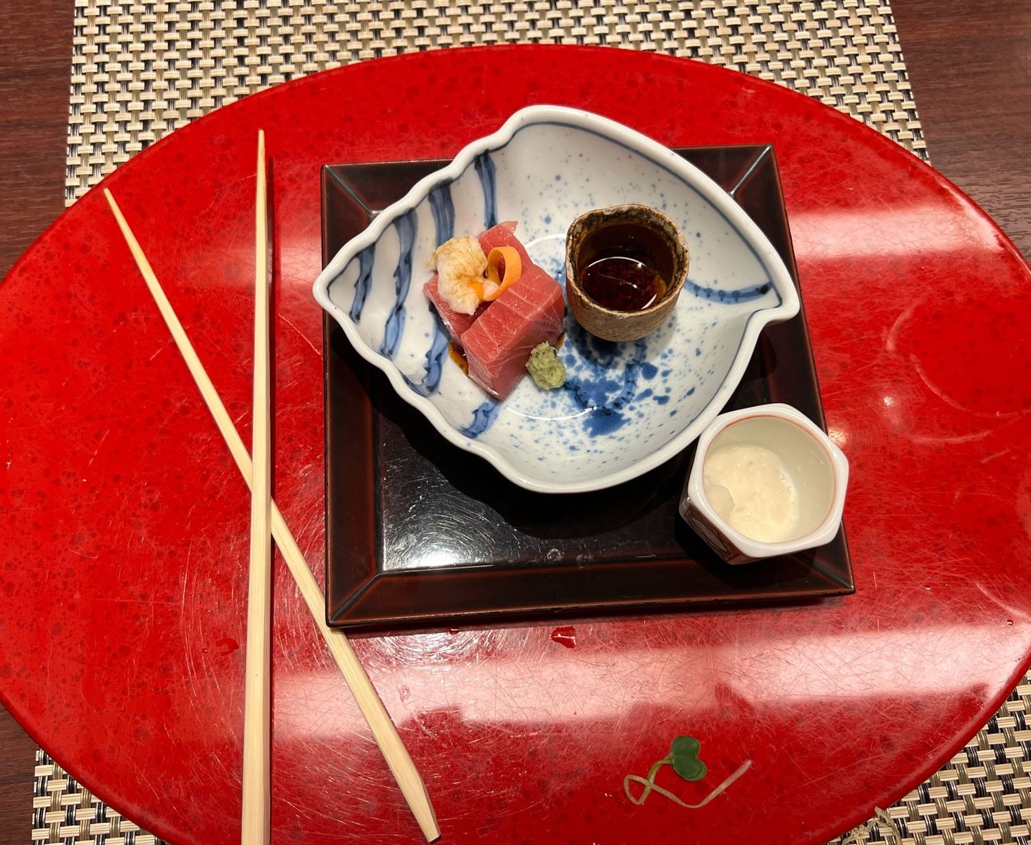 A stylish Japanese meal presentation with sauces and chopsticks on a vibrant red charger plate.