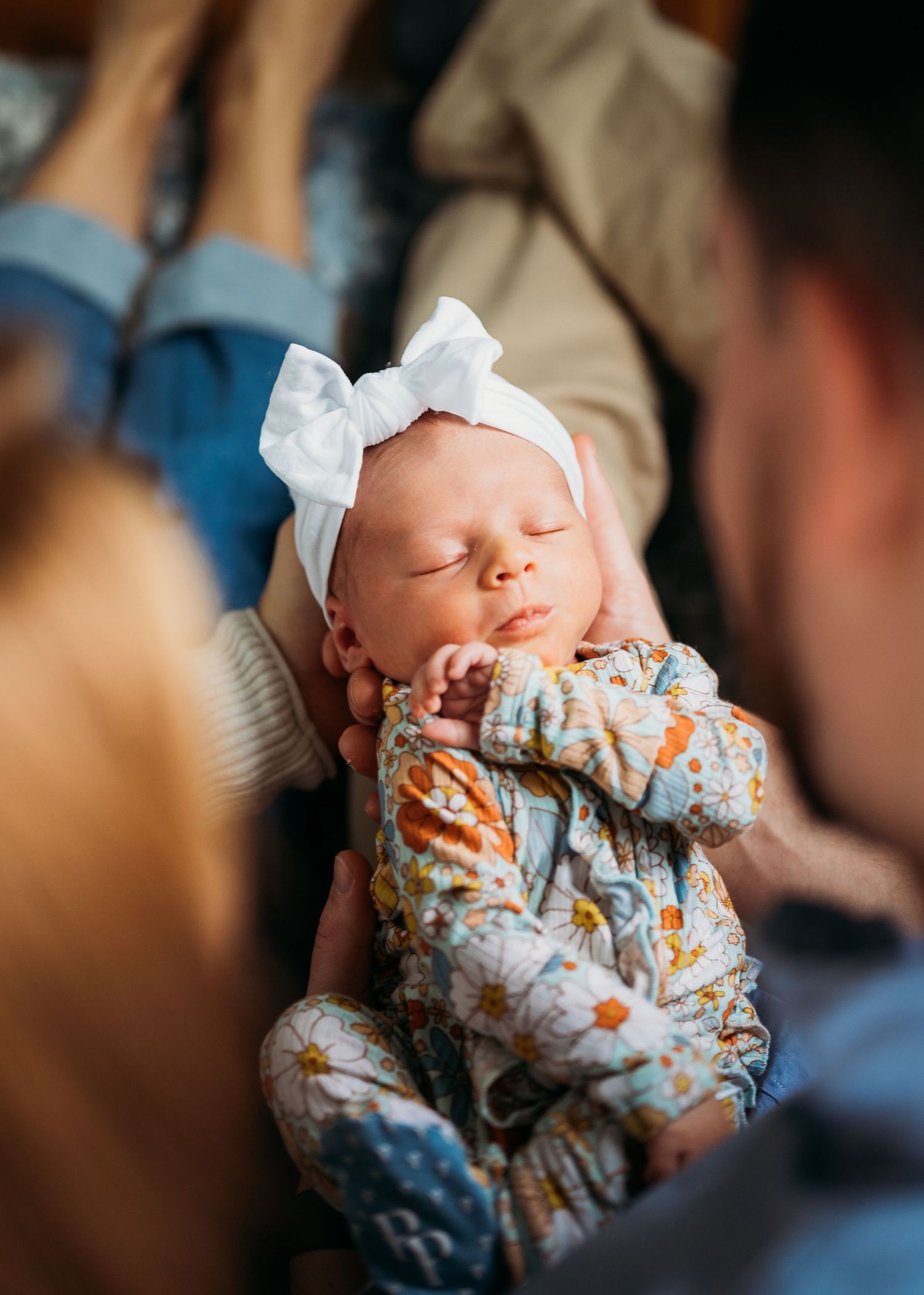 Sleeping newborn in floral print outfit and white bow headband.