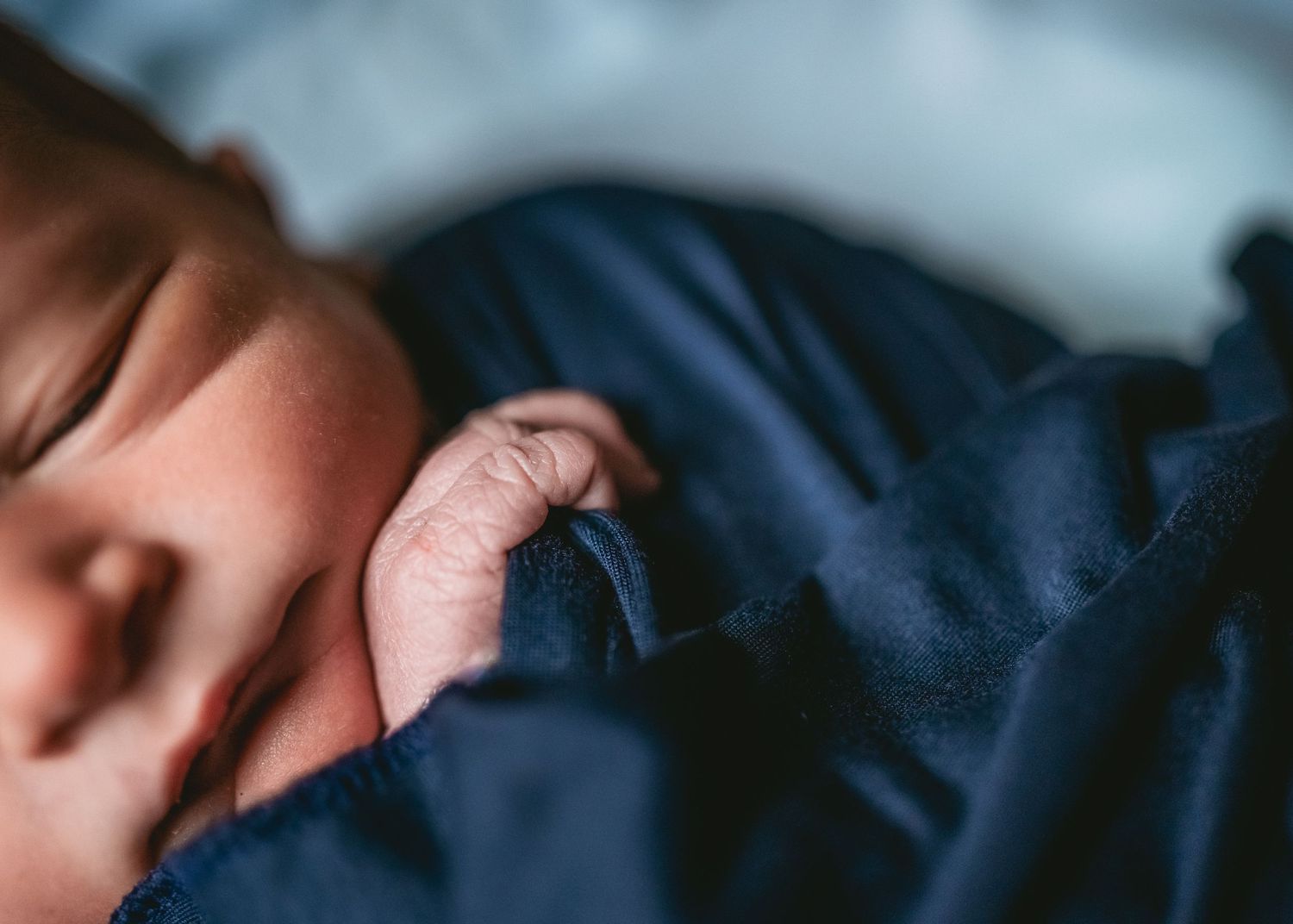 Close-up portrait of a sleeping newborn in dark blue clothing.