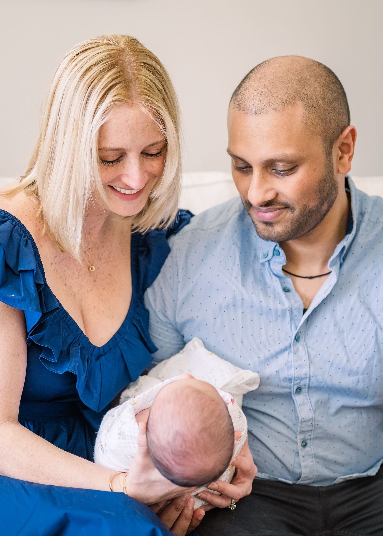 Parents in blue and grey attire sharing tender moment while holding newborn baby.