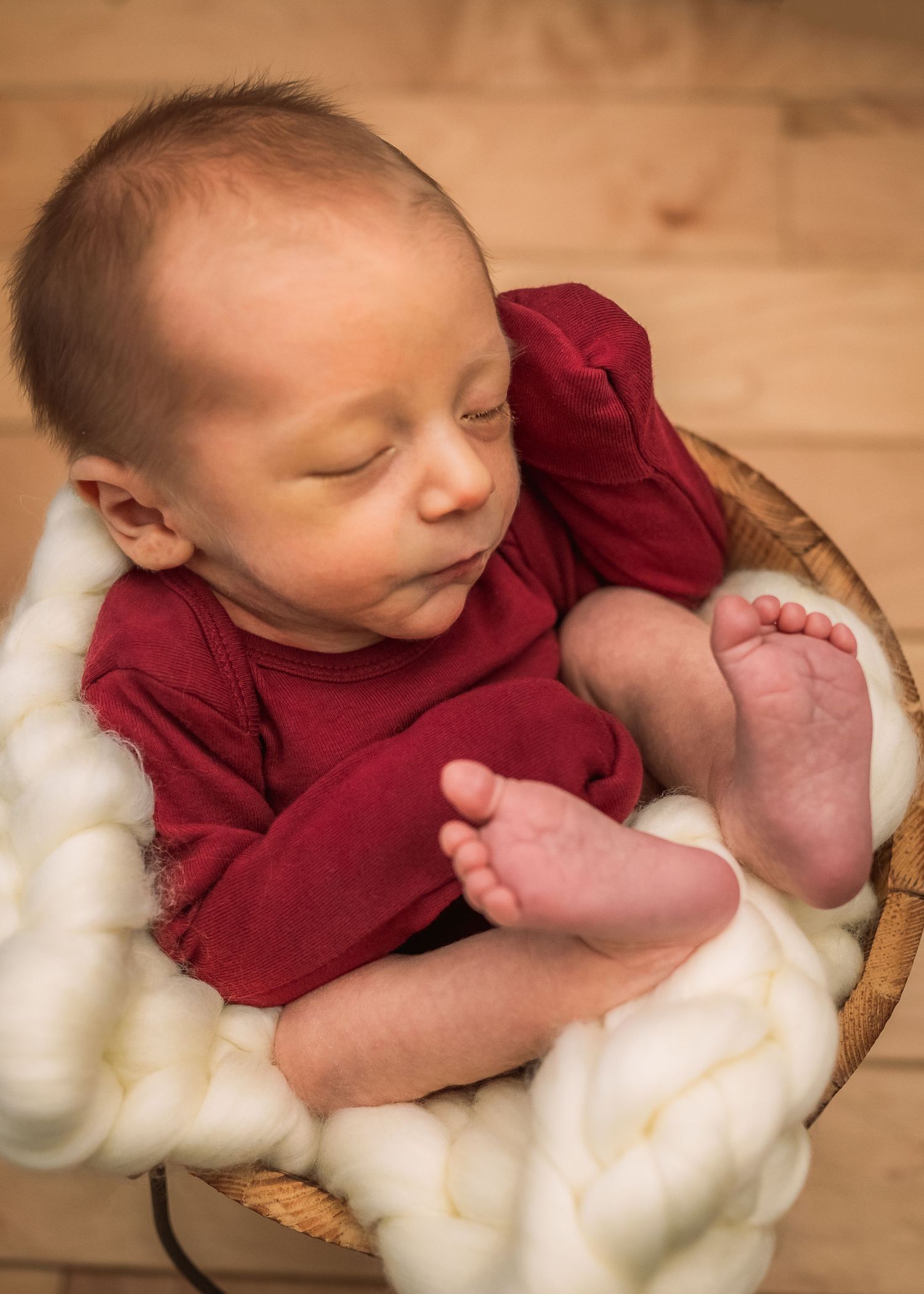 Sleeping baby in red outfit nestled in basket with white wool padding.