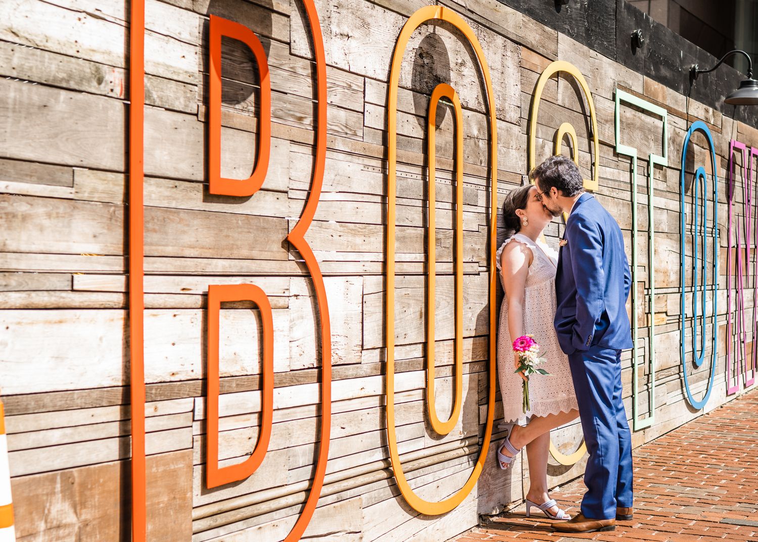 A couple poses against colorful street art spelling BOSTON on a brick wall.