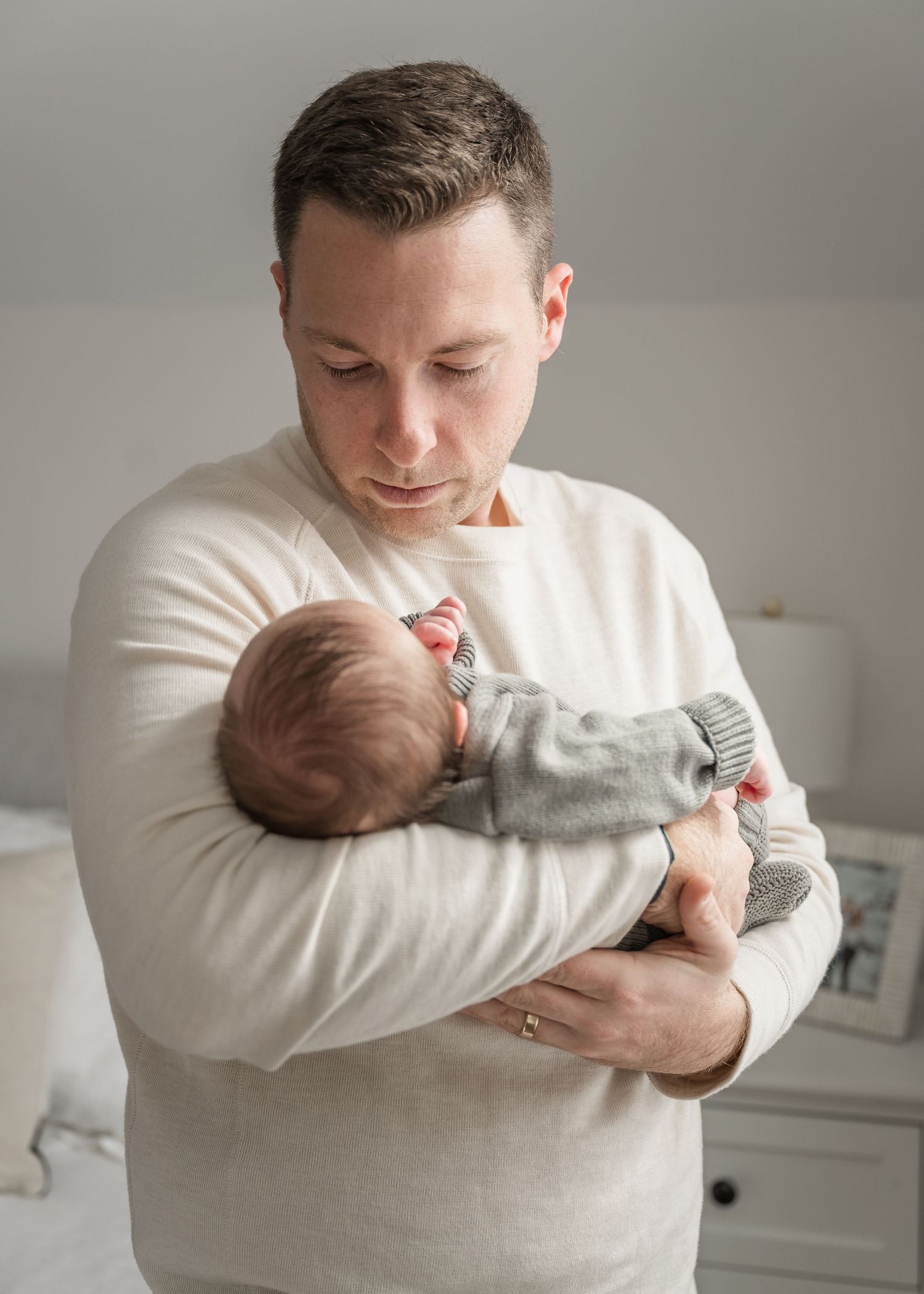 A tender moment as a parent in a cream sweater cradles their sleeping newborn baby wearing a gray outfit.