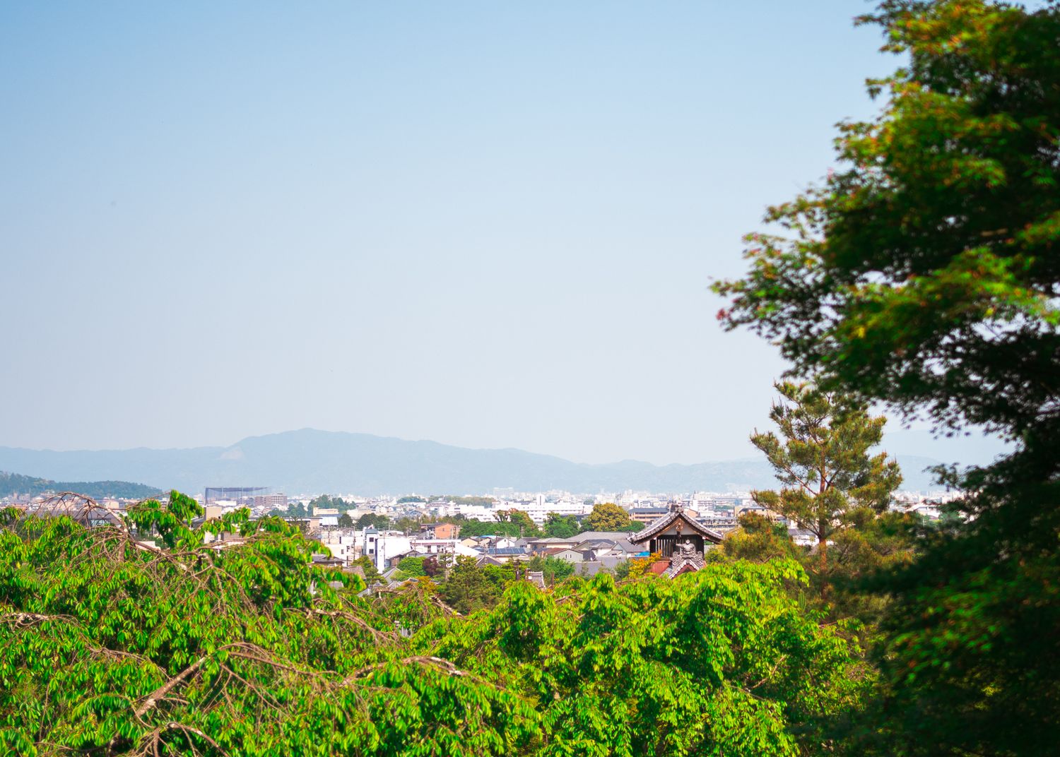 Aerial view of a Japanese city with mountains and traditional architecture visible in the distance.