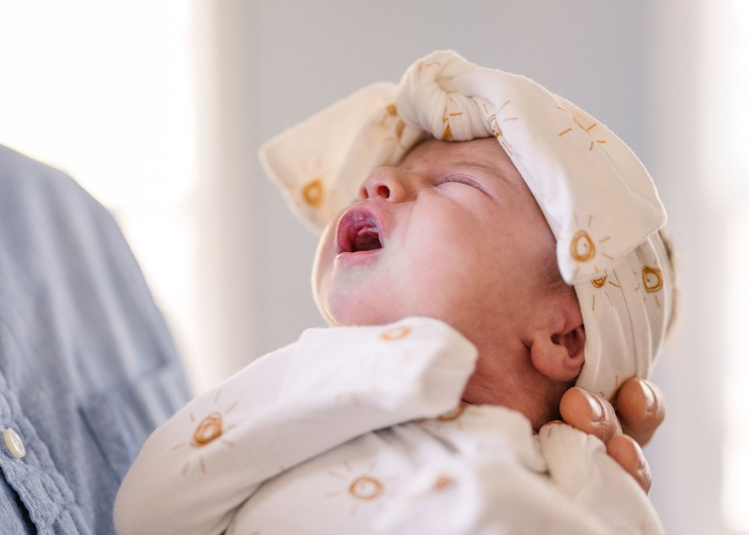 Baby wearing cream patterned outfit stretches and yawns.