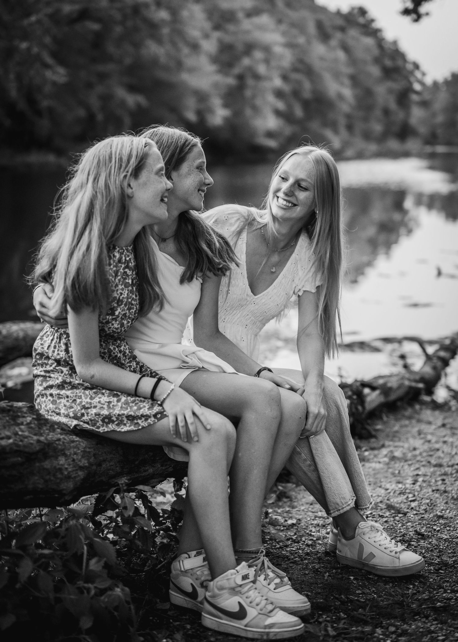 Black and white photo of three people sitting on rocks by a lake sharing joyful conversation.