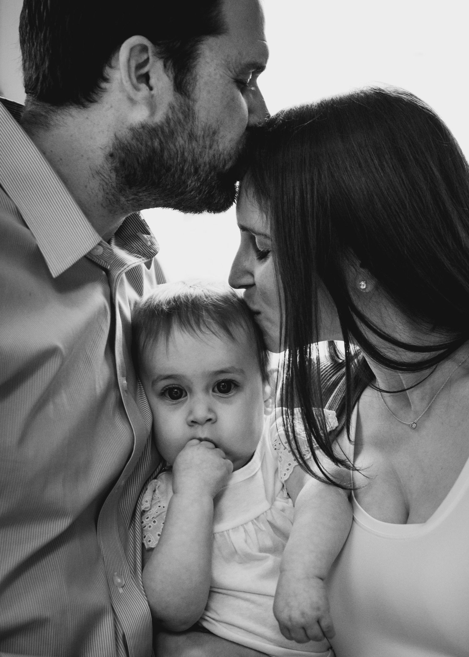 An intimate black and white family portrait showing affectionate parents with their young child.