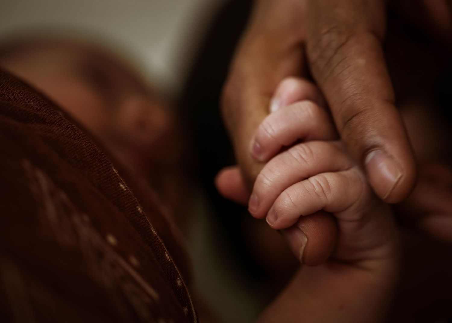 Close up of tiny baby hand being held against brown fabric.