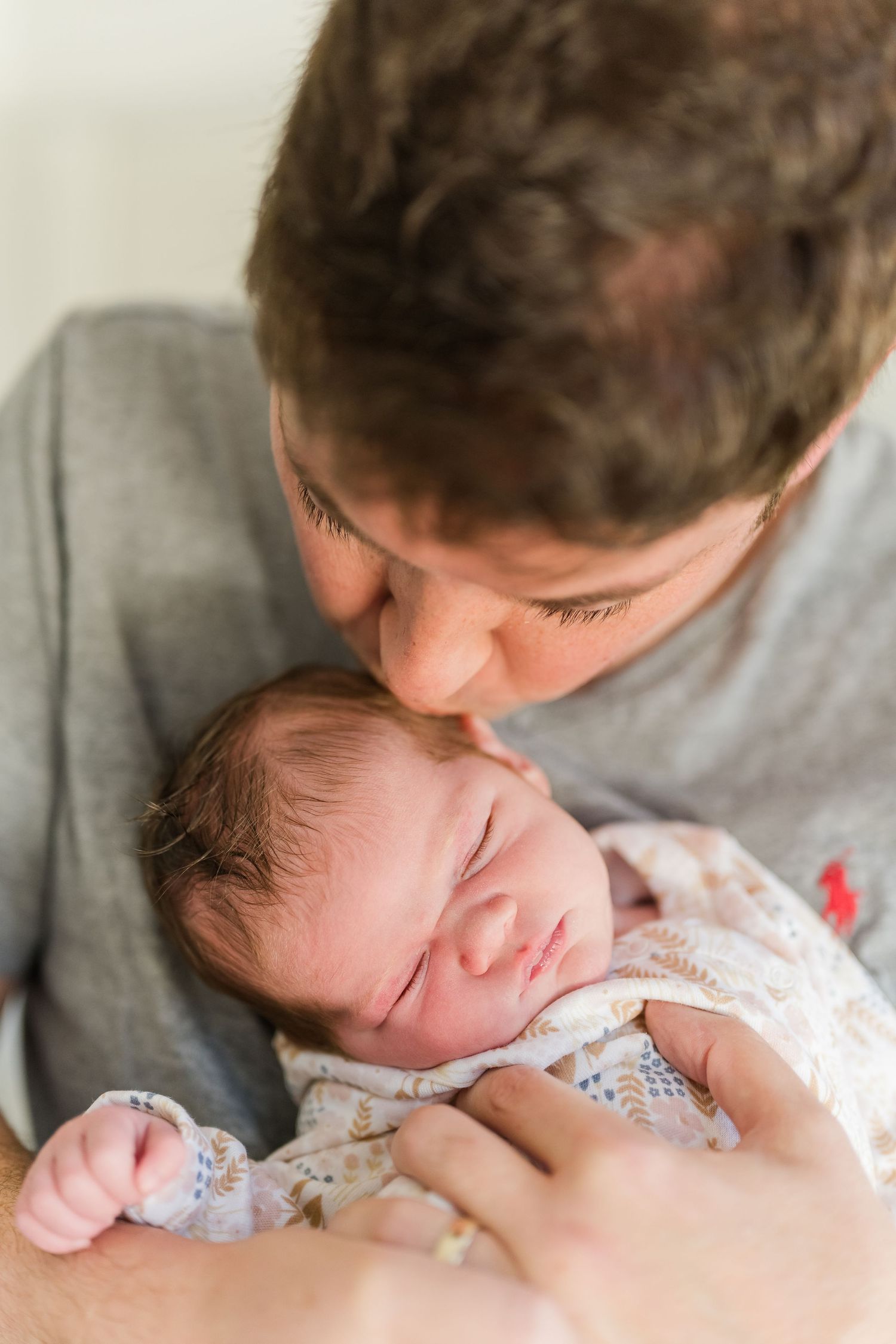 A tender moment shows a sleeping newborn baby in white floral clothing being held and kissed gently.