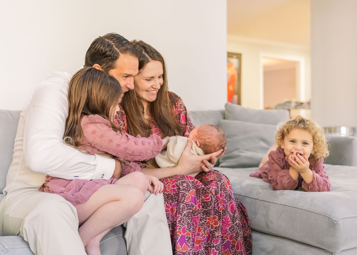Happy family moment on couch with newborn baby and coordinated pink clothing.