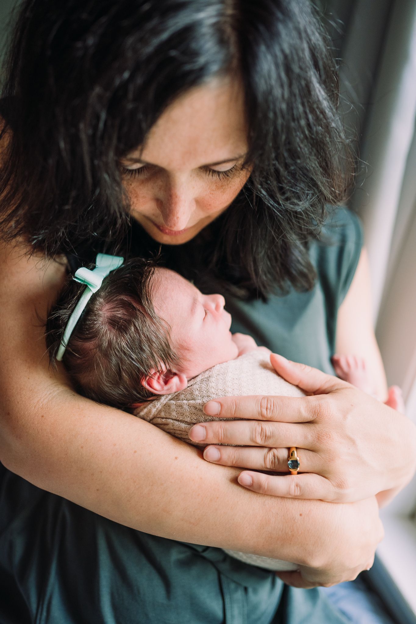 Tender moment between mother and newborn baby by window light.