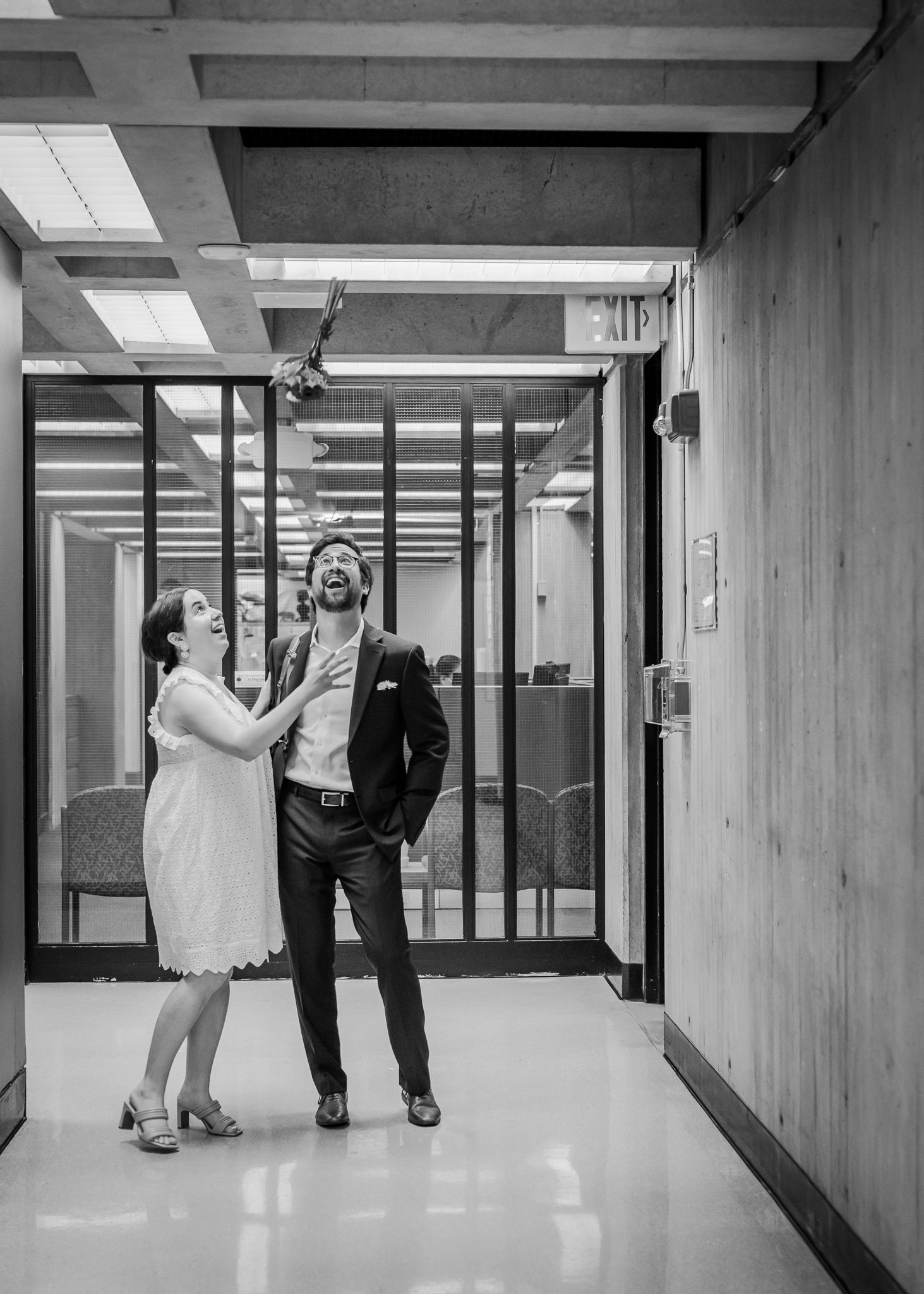 A candid black and white moment of a couple dancing and laughing in a modern hallway.