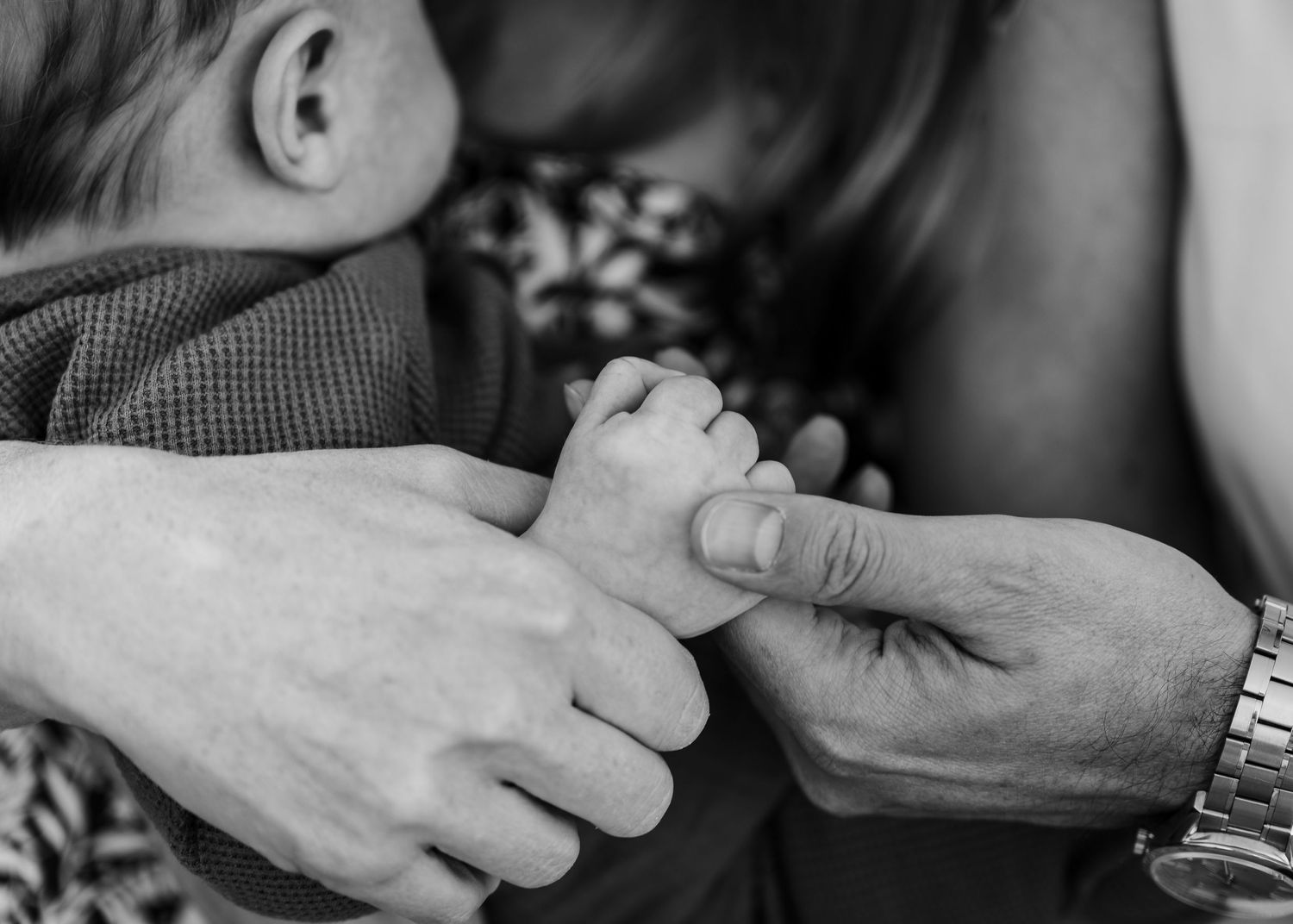 A close-up black and white photo showing tiny baby fingers being gently held by adult hands.