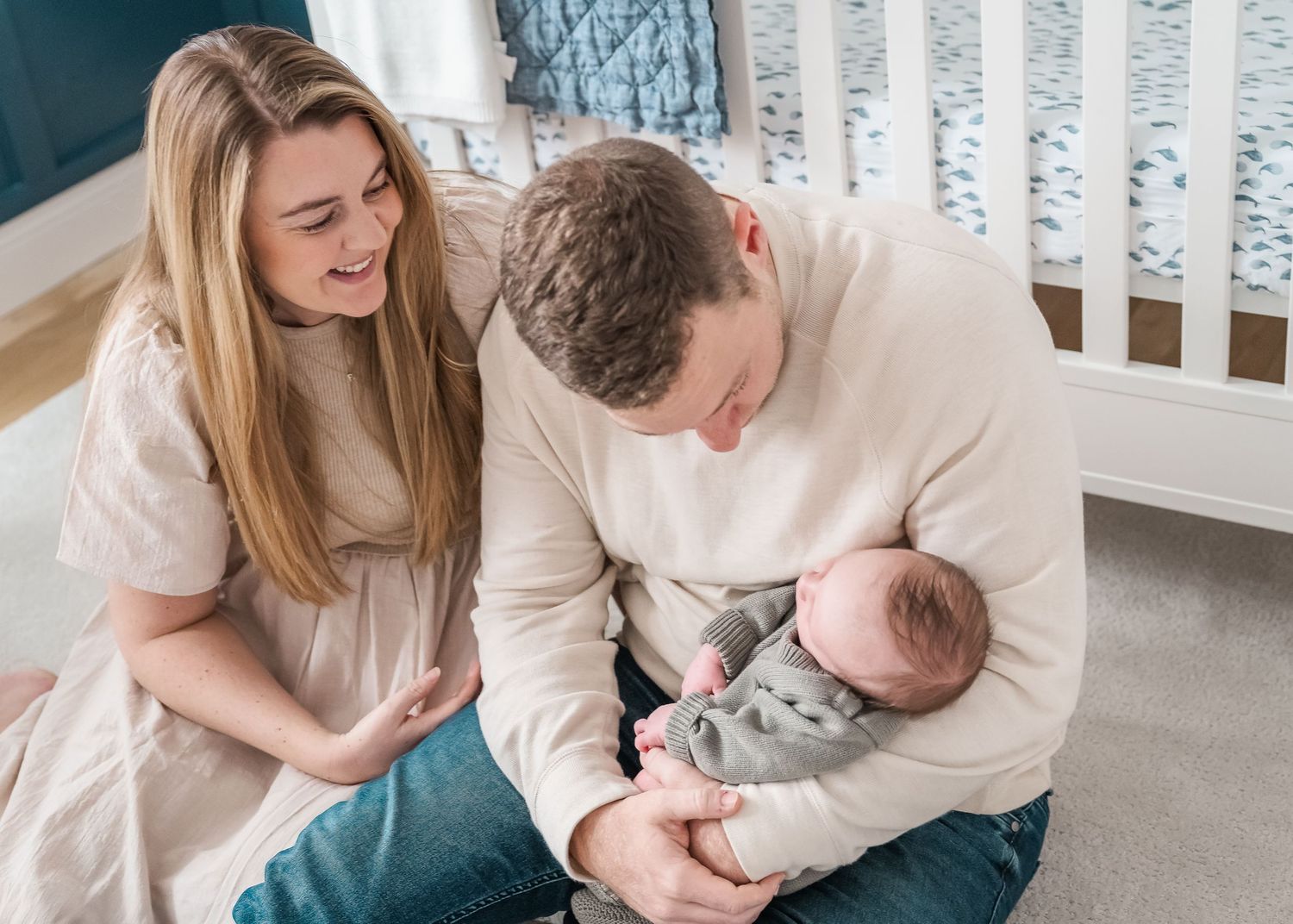 Parents sharing a tender moment with their newborn baby in a nursery with a white crib.