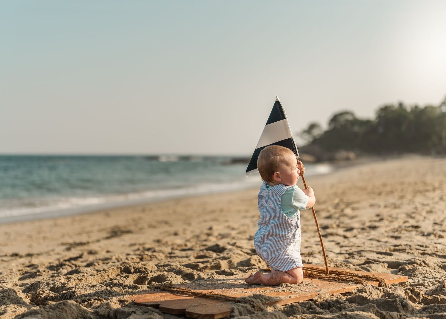 A baby crawls on a sandy beach at sunset while exploring the shoreline and sand.