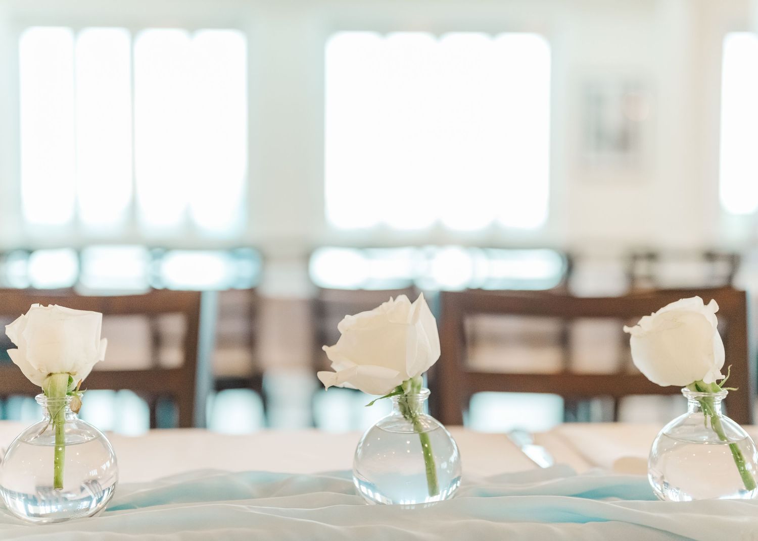 Row of delicate white roses in crystal vases lined up on an elegant table setting.