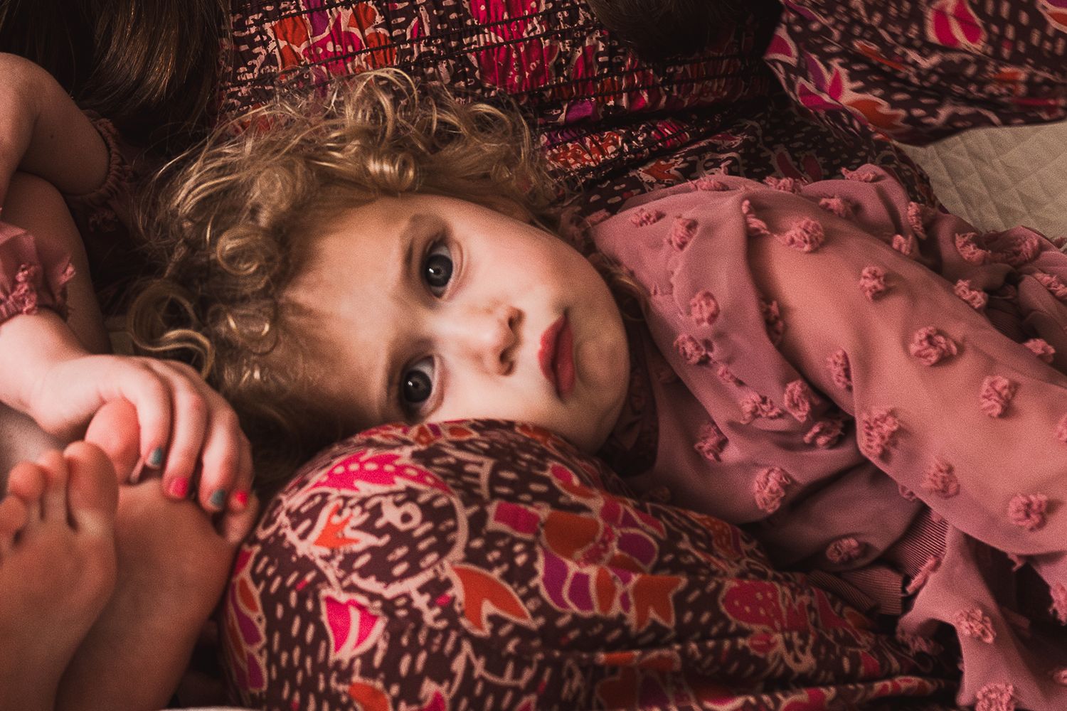 Child in pink ruffled dress lying on patterned fabric in warm lighting.