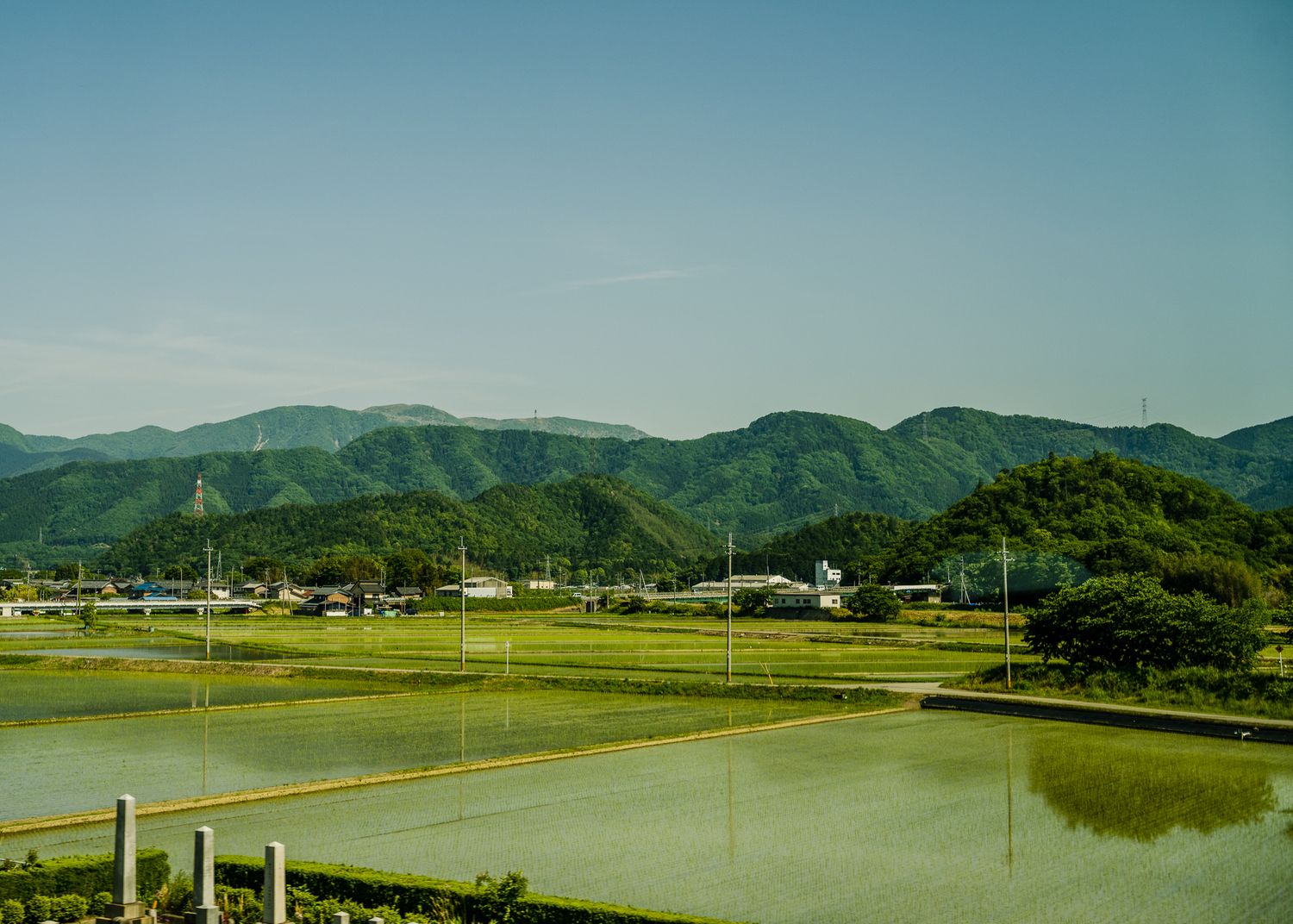 Scenic Japanese countryside landscape with green mountains and flooded rice fields under blue skies.