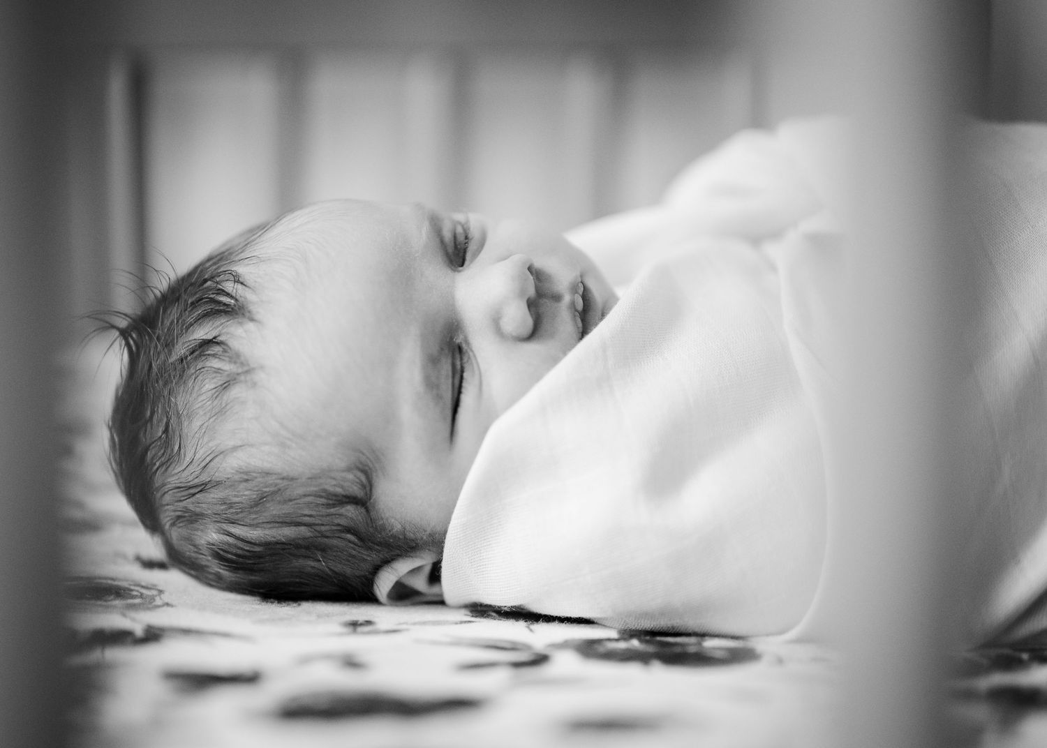 A sleeping infant peacefully rests swaddled in white blankets captured in black and white photography.