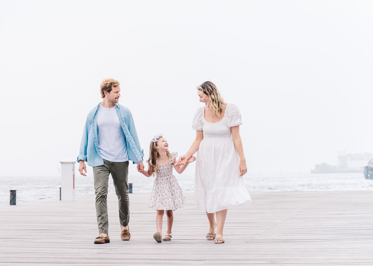 Family holding hands while taking a stroll together on a waterfront boardwalk.