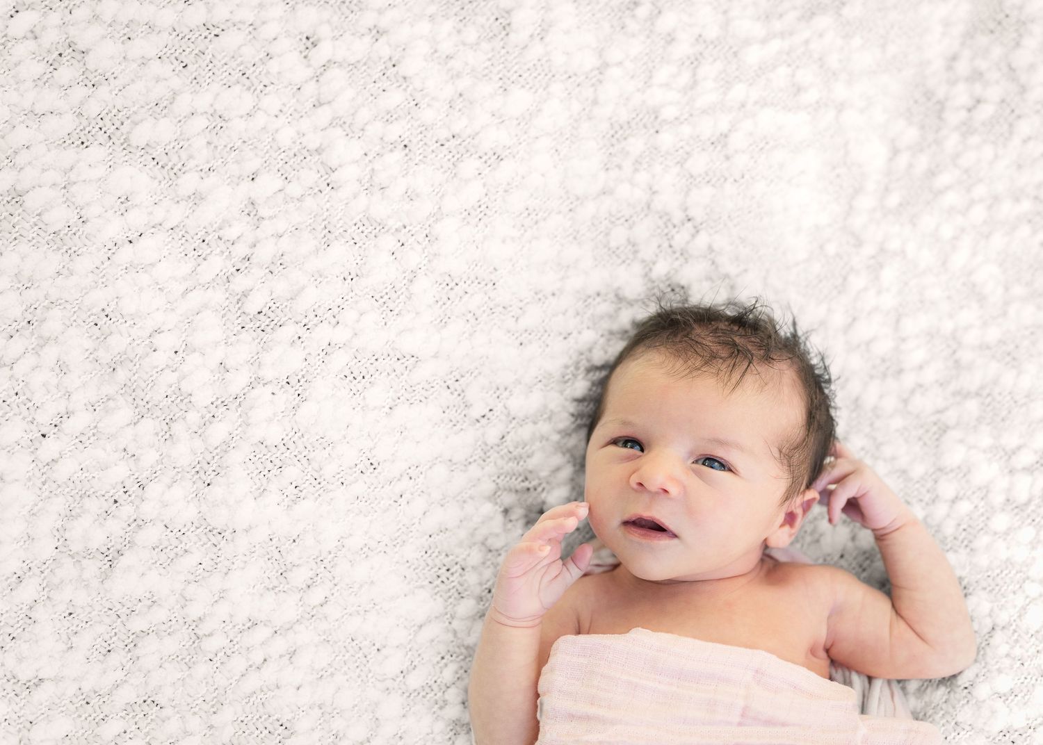Baby lying on white fluffy blanket with curious expression.