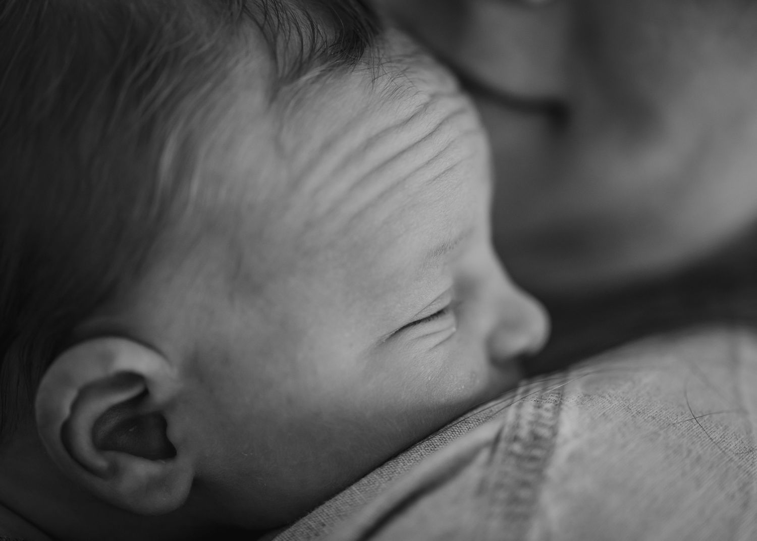 Black and white portrait of sleeping baby on parent's shoulder.