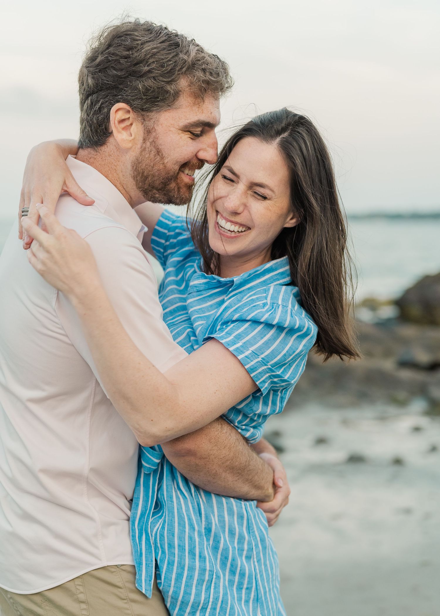 Couple embracing and laughing on rocky beach at sunset.