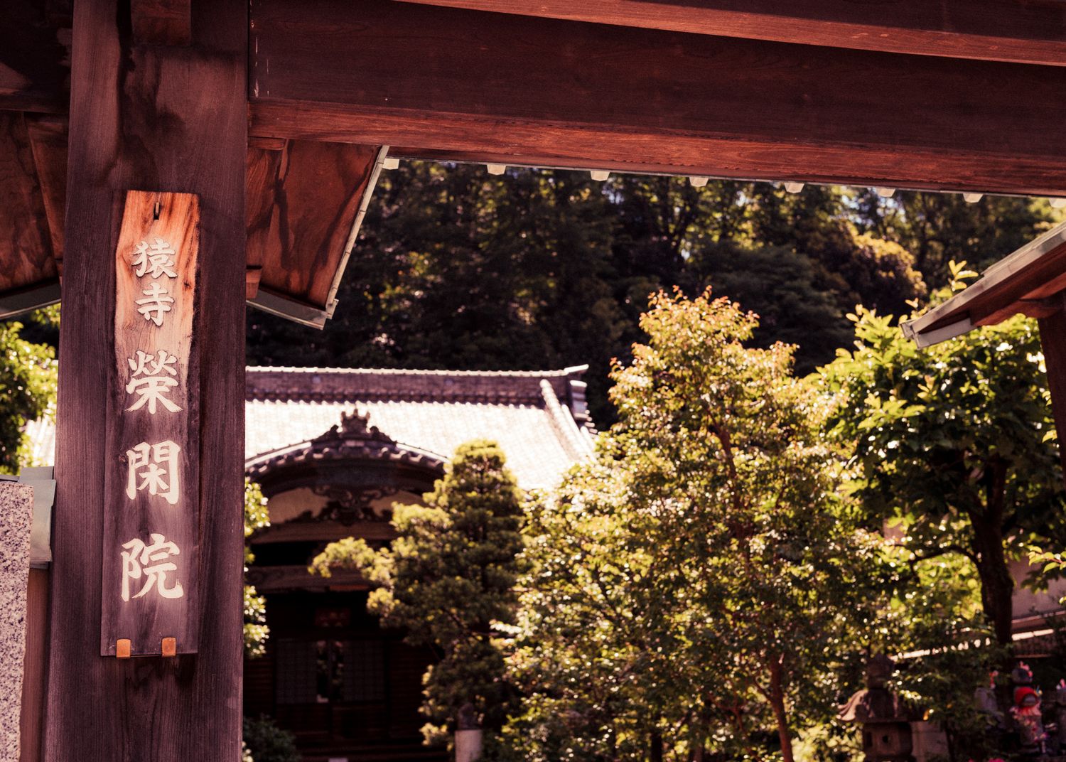 Traditional Japanese temple entrance gate with wooden sign and green foliage.