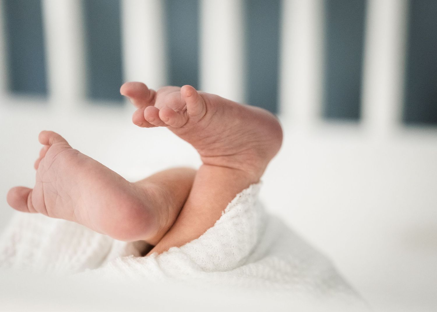 Baby's tiny feet resting on white bedding against crib background.