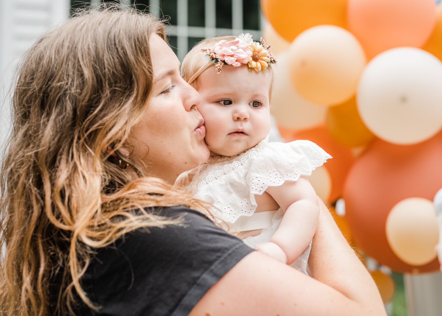 Candid moment with orange and white balloon decorations in background.