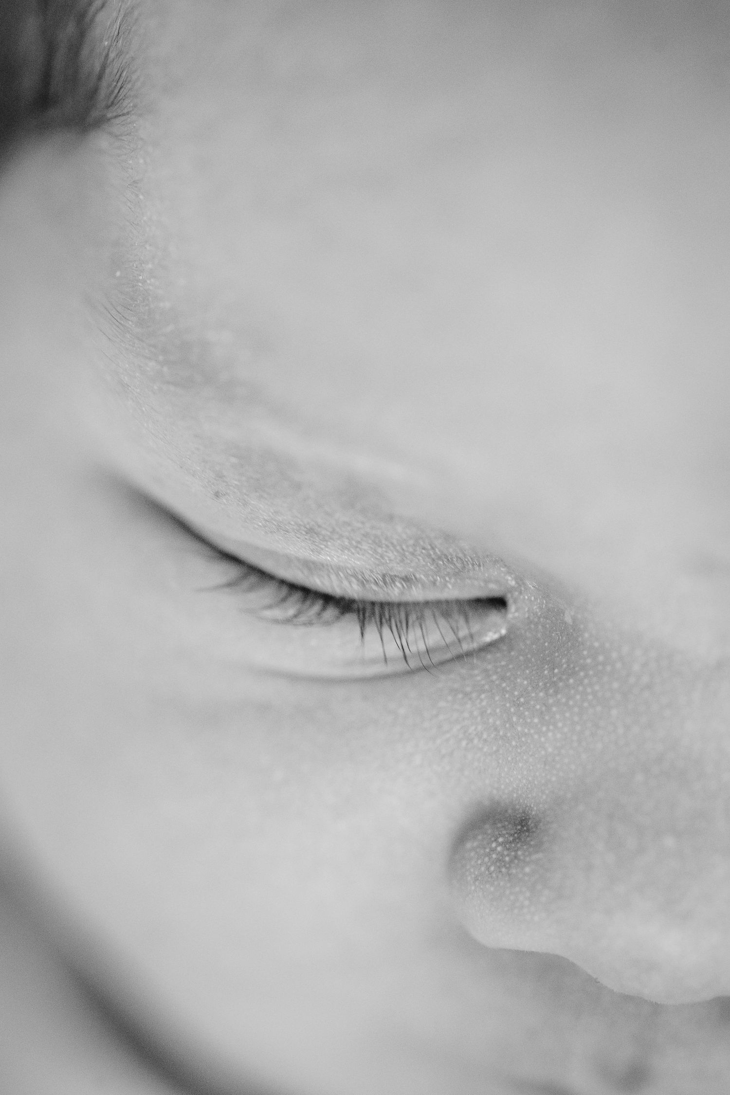 An extreme close-up black and white photo shows a delicate closed eyelid with fine eyelashes against pale skin.