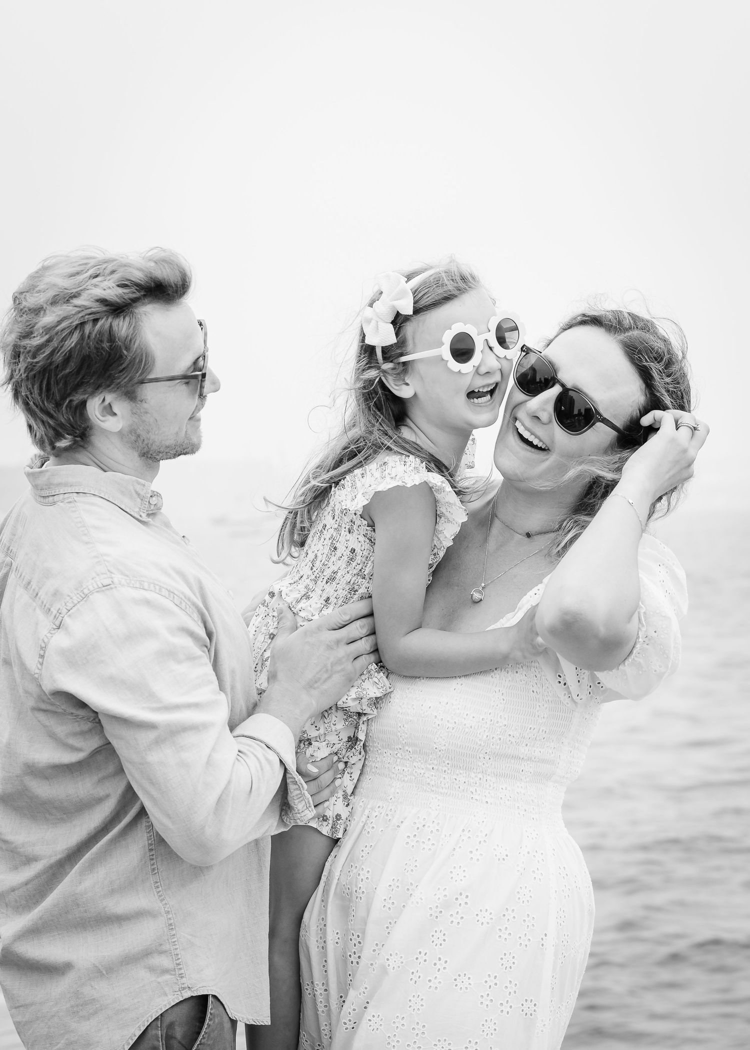 Black and white portrait of a family wearing sunglasses and sharing laughs by the water.
