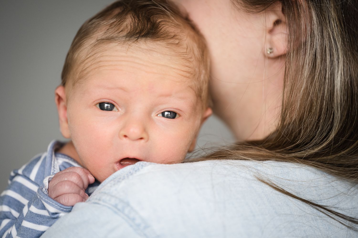 Baby resting on parent's shoulder wearing striped clothing in closeup portrait.