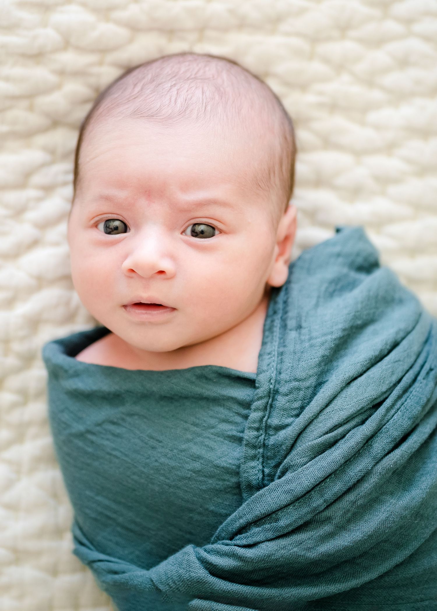 Baby swaddled in teal fabric on white blanket.