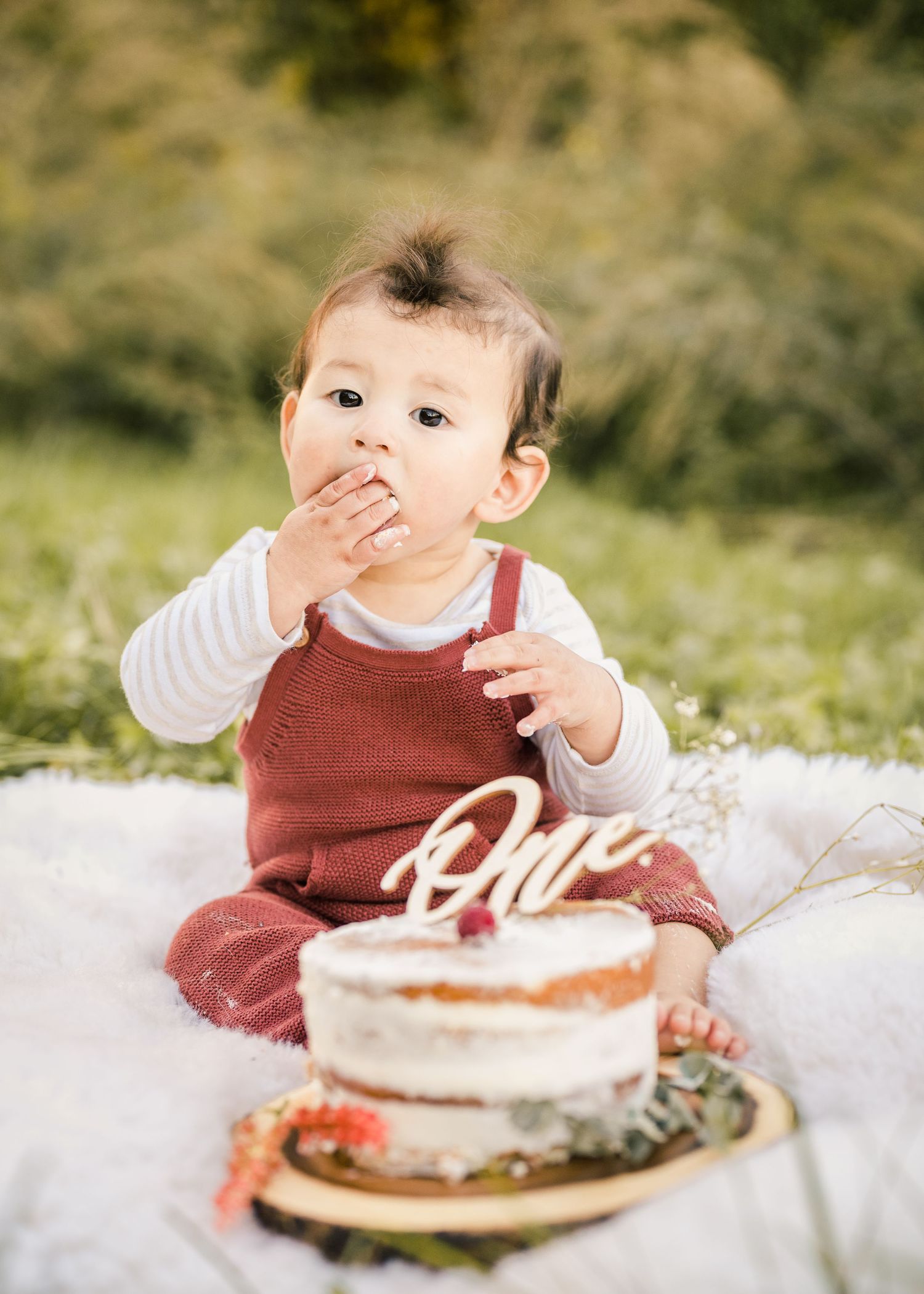 Baby tasting cake during first birthday photoshoot with rustic decorations outdoors.