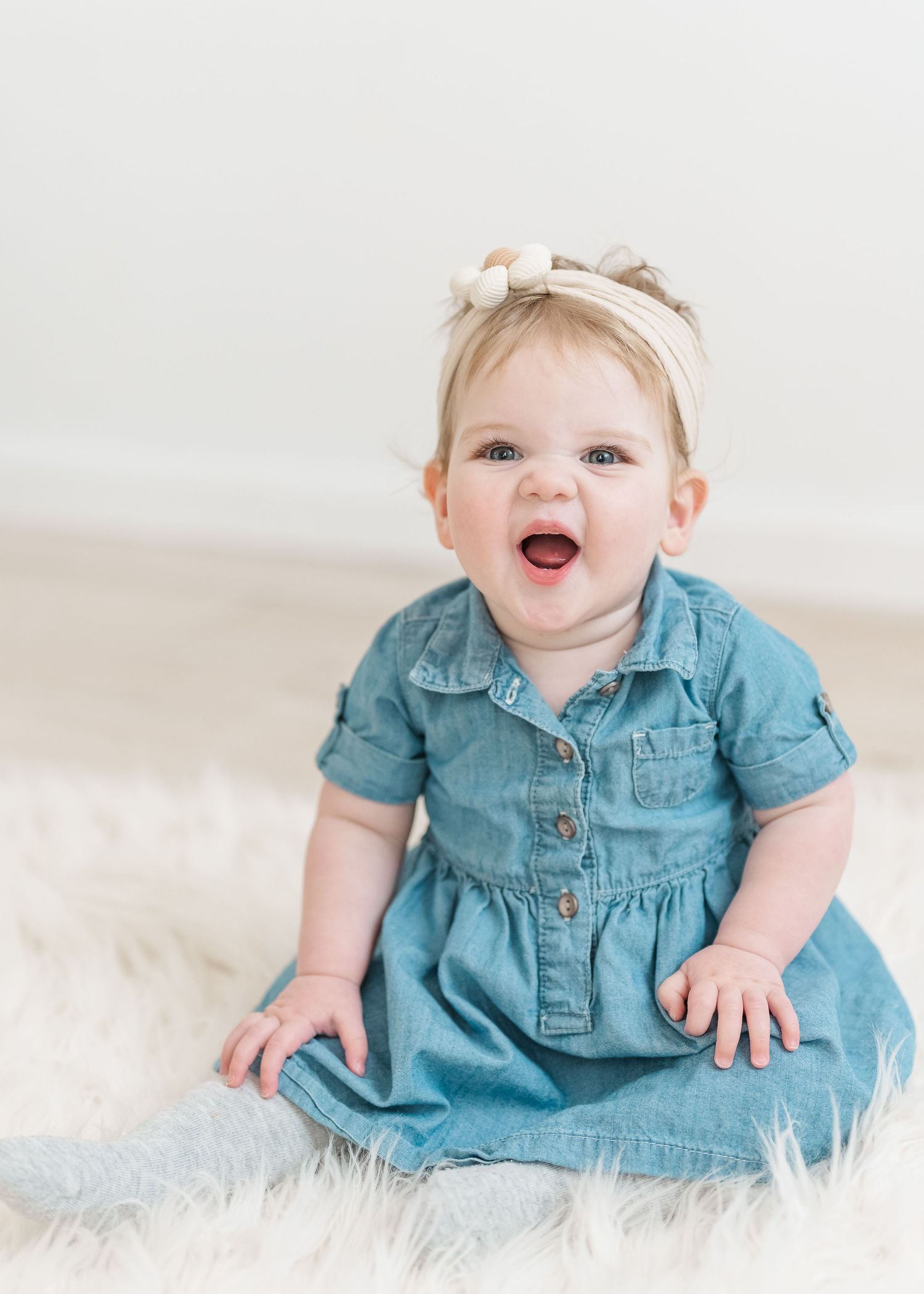 Baby in denim dress sits and smiles on white fluffy rug in progressive developmental stages.