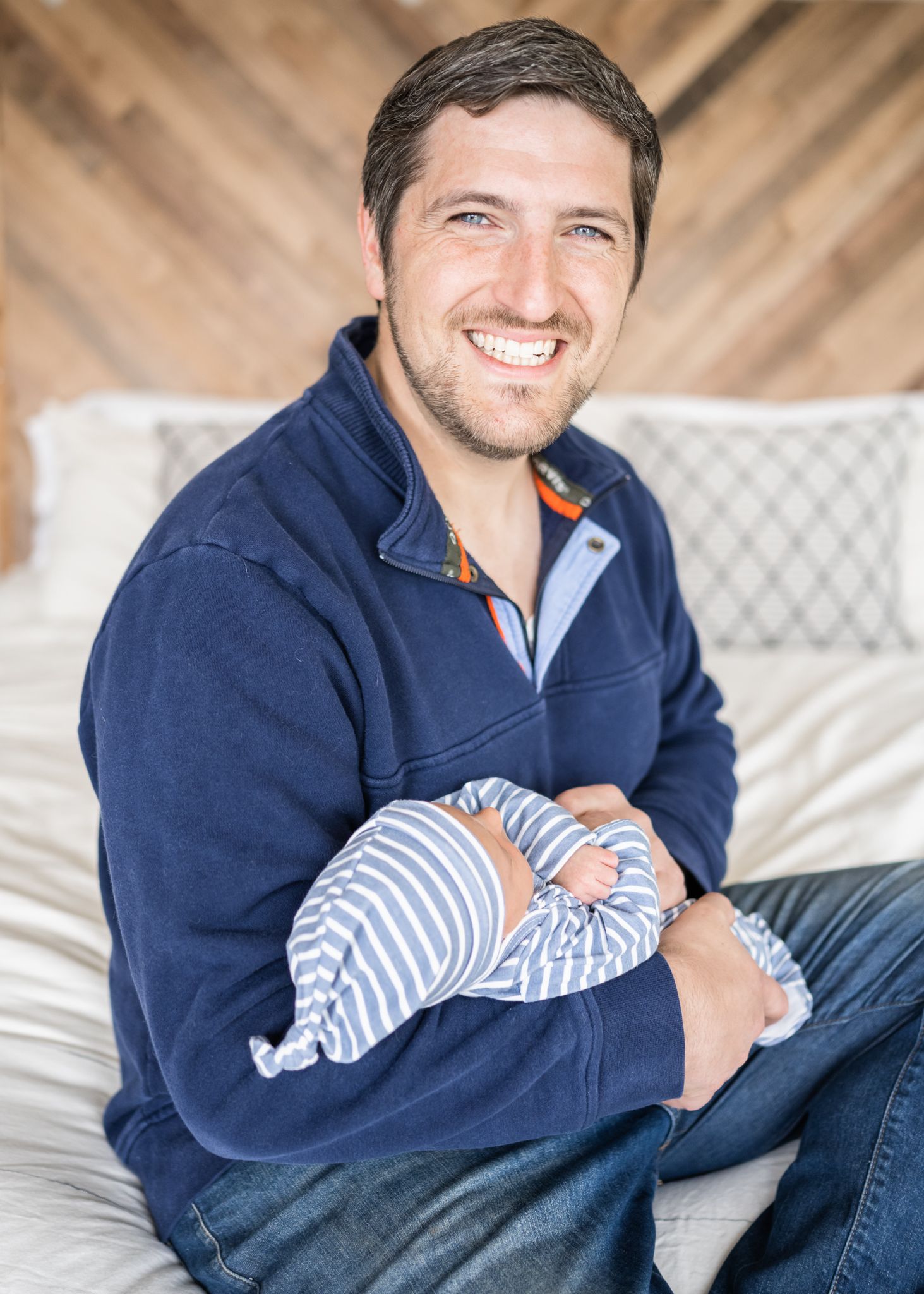 Relaxed scene of a navy fleece-wearing adult holding a sleeping baby in striped clothing.