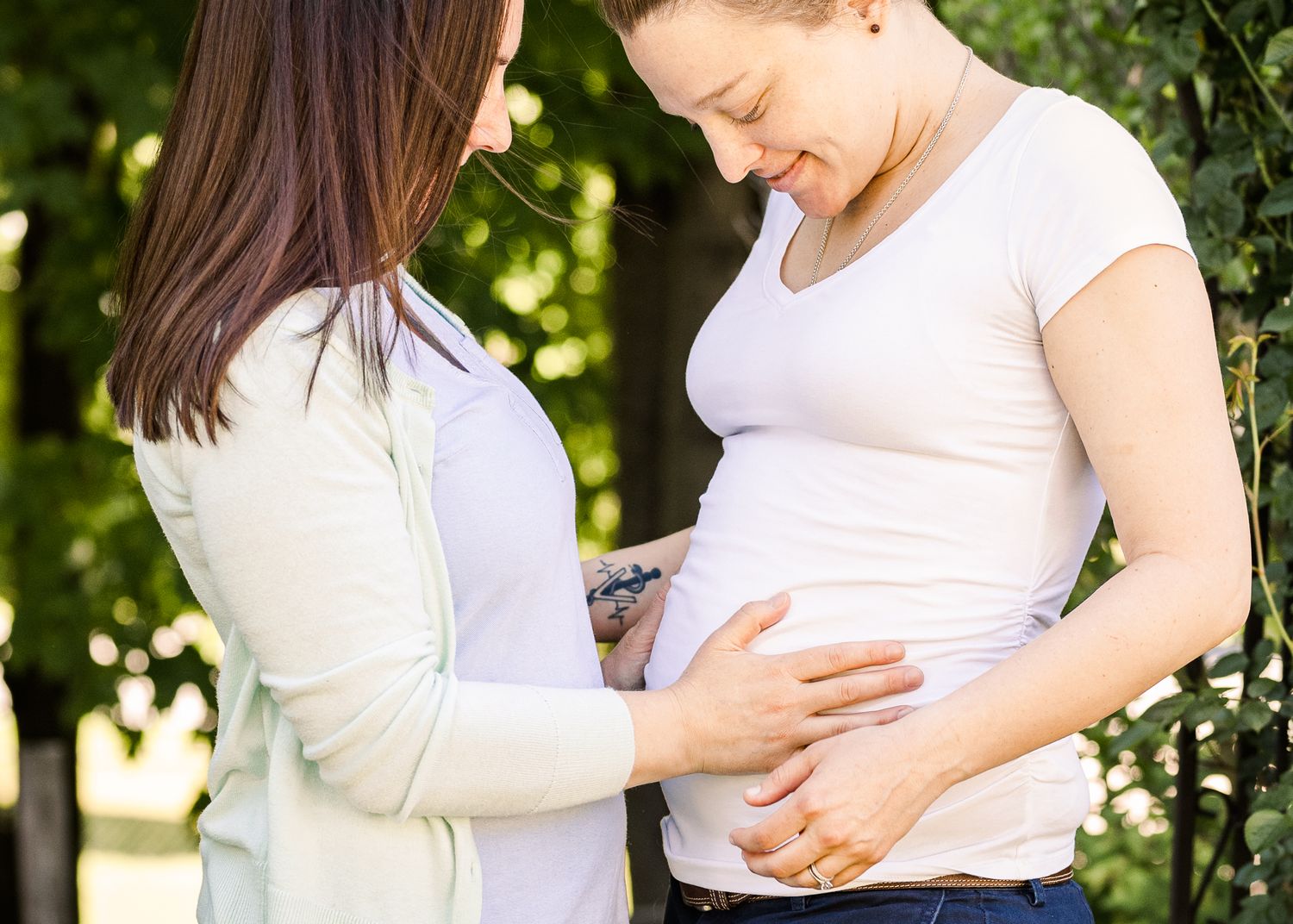 A gentle moment captured as hands rest on a pregnant belly in a sunlit garden setting.