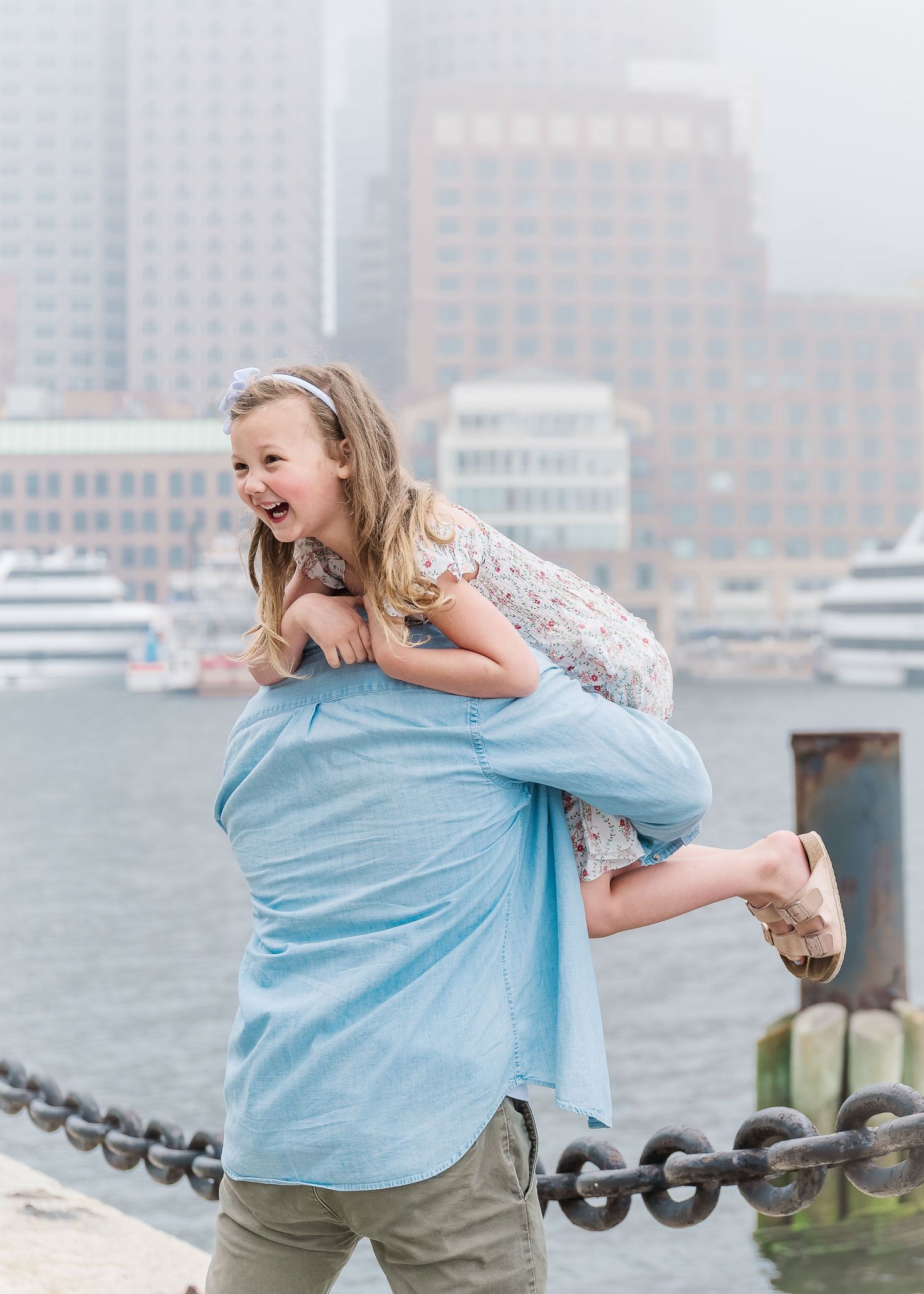 Playful moment captured on a harbor walkway with city buildings shrouded in fog.