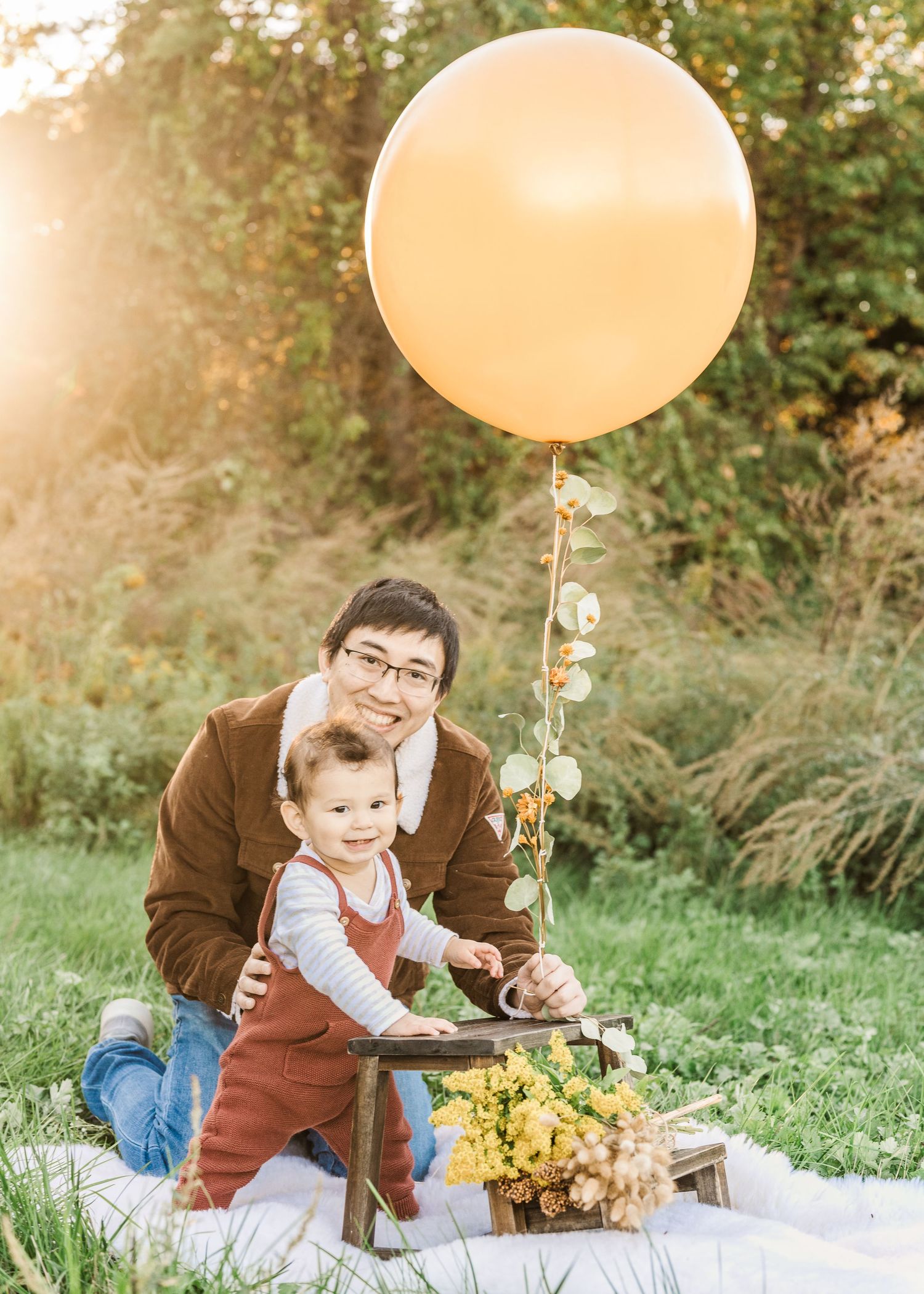 Outdoor photo with large peach balloon, rustic decorations and yellow flowers on white blanket.